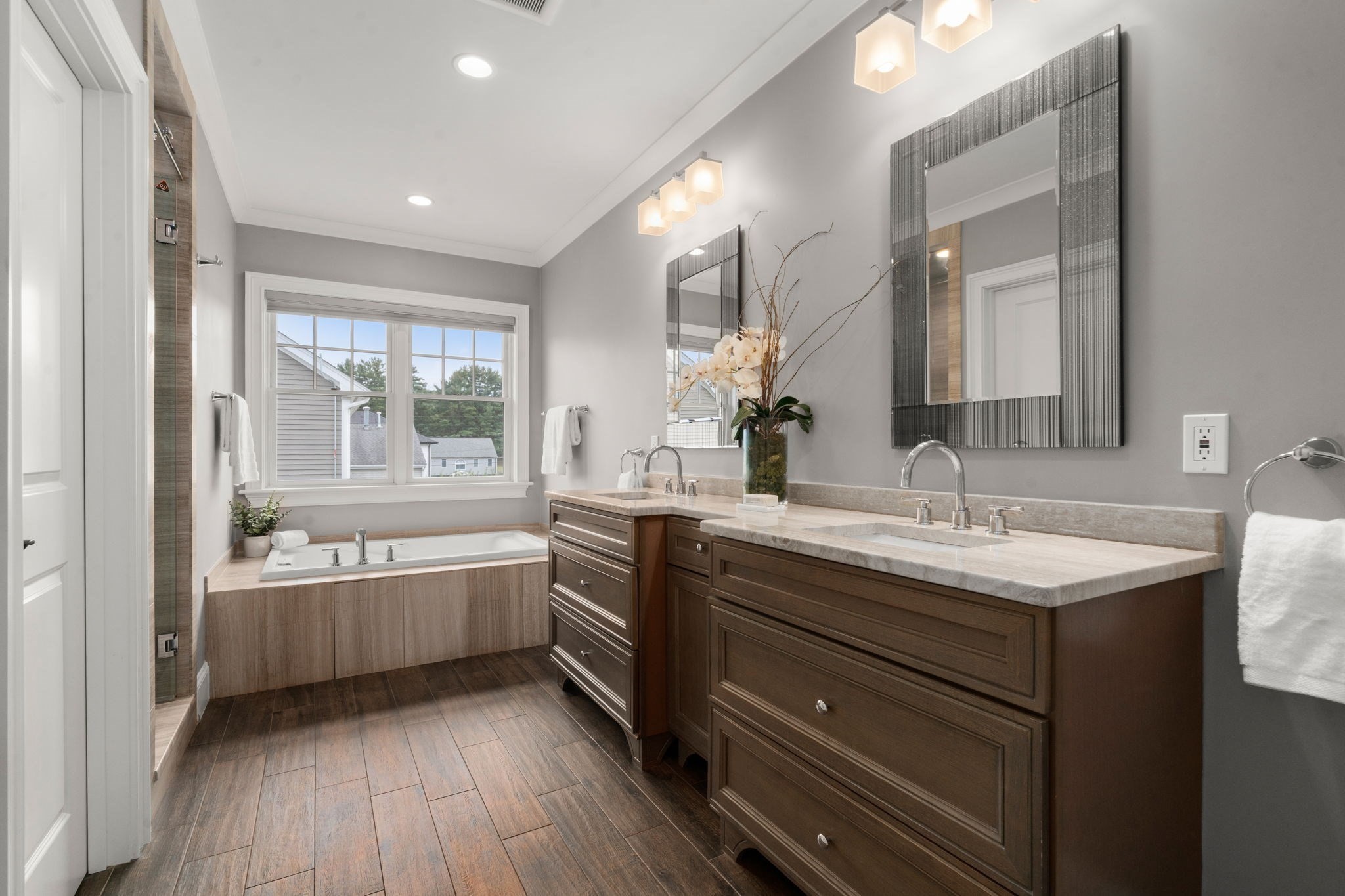 Bathroom with a dark wood double vanity and soaking tub beneath a large window.