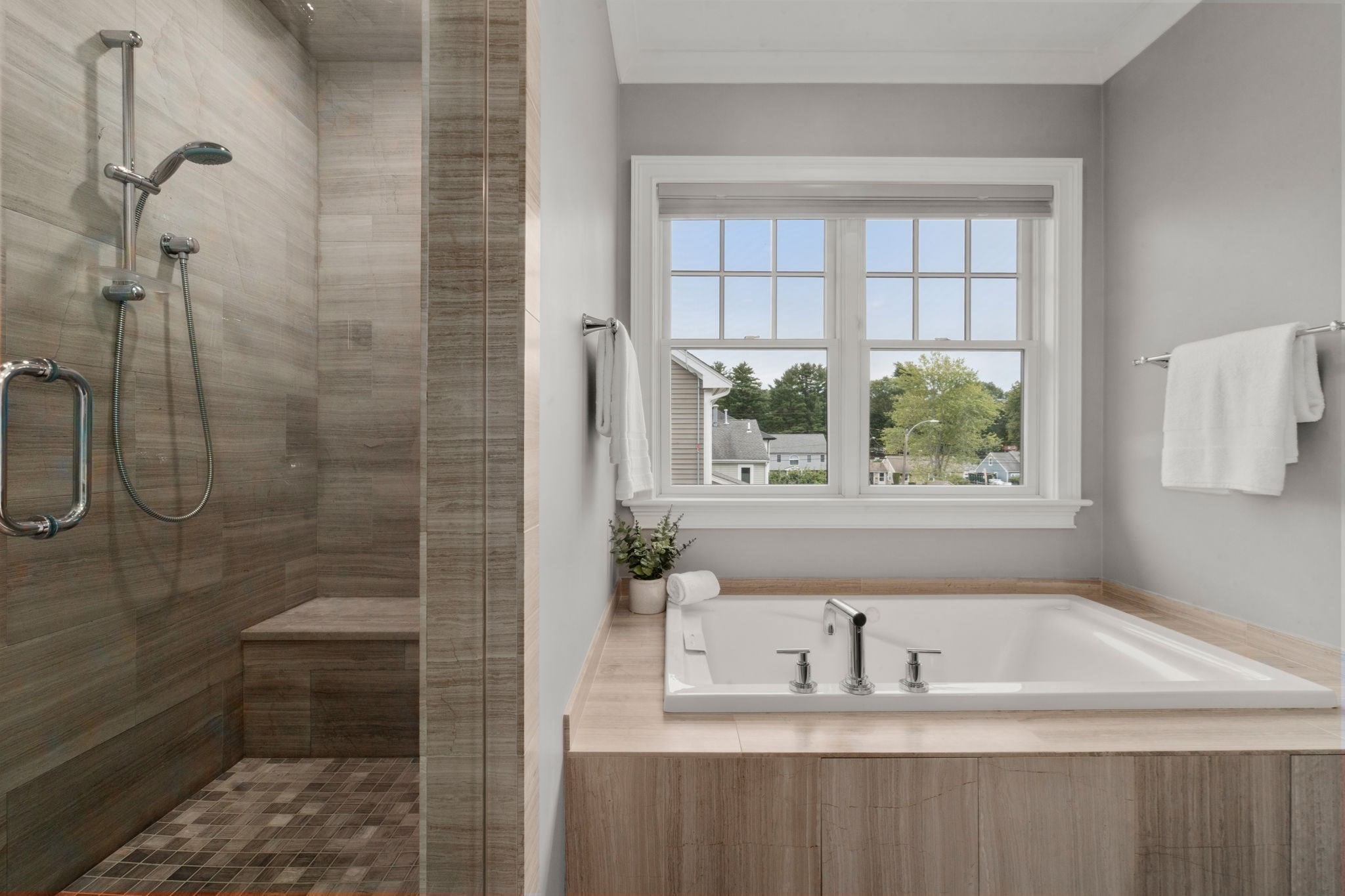 Bathroom with a tiled walk-in shower and soaking tub beneath a large window.