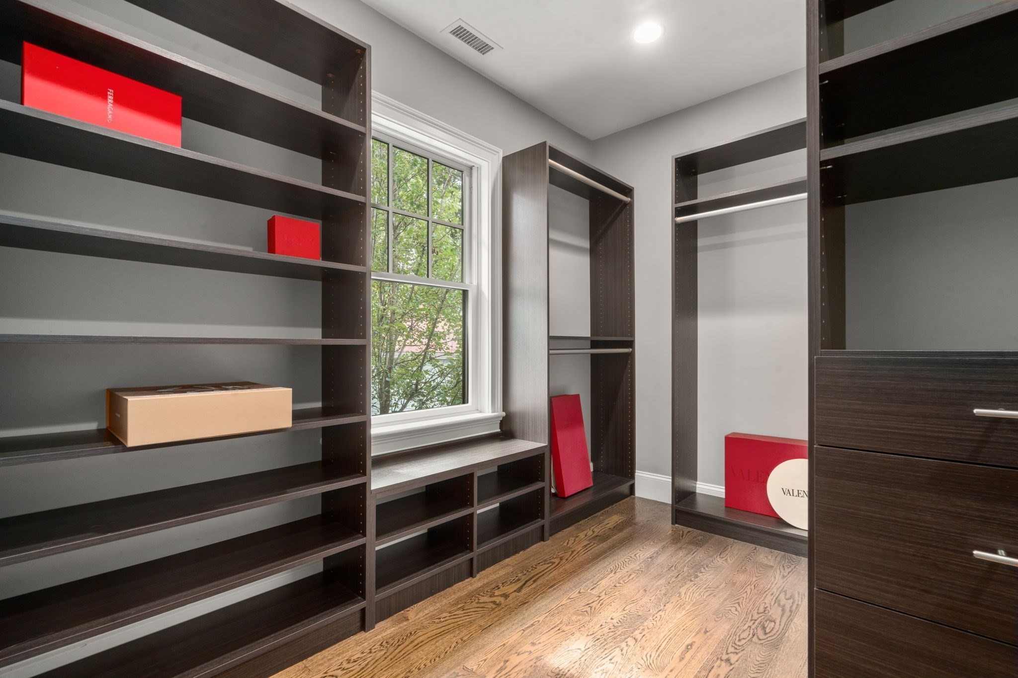 Walk-in closet with dark wood shelving, drawers, hardwood floors, and a large window.