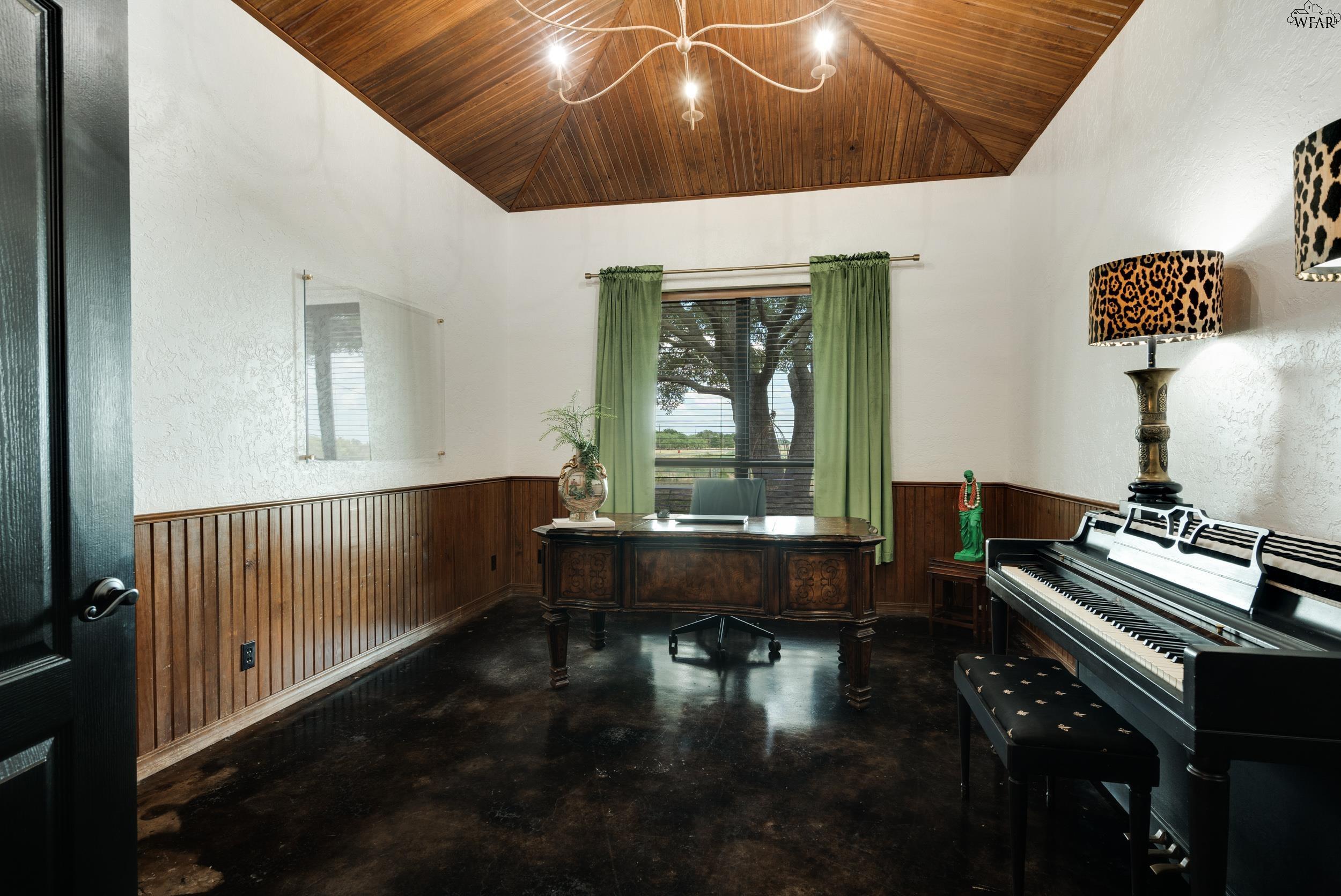Home office with a carved wooden desk, grand piano, and vaulted wood ceiling.