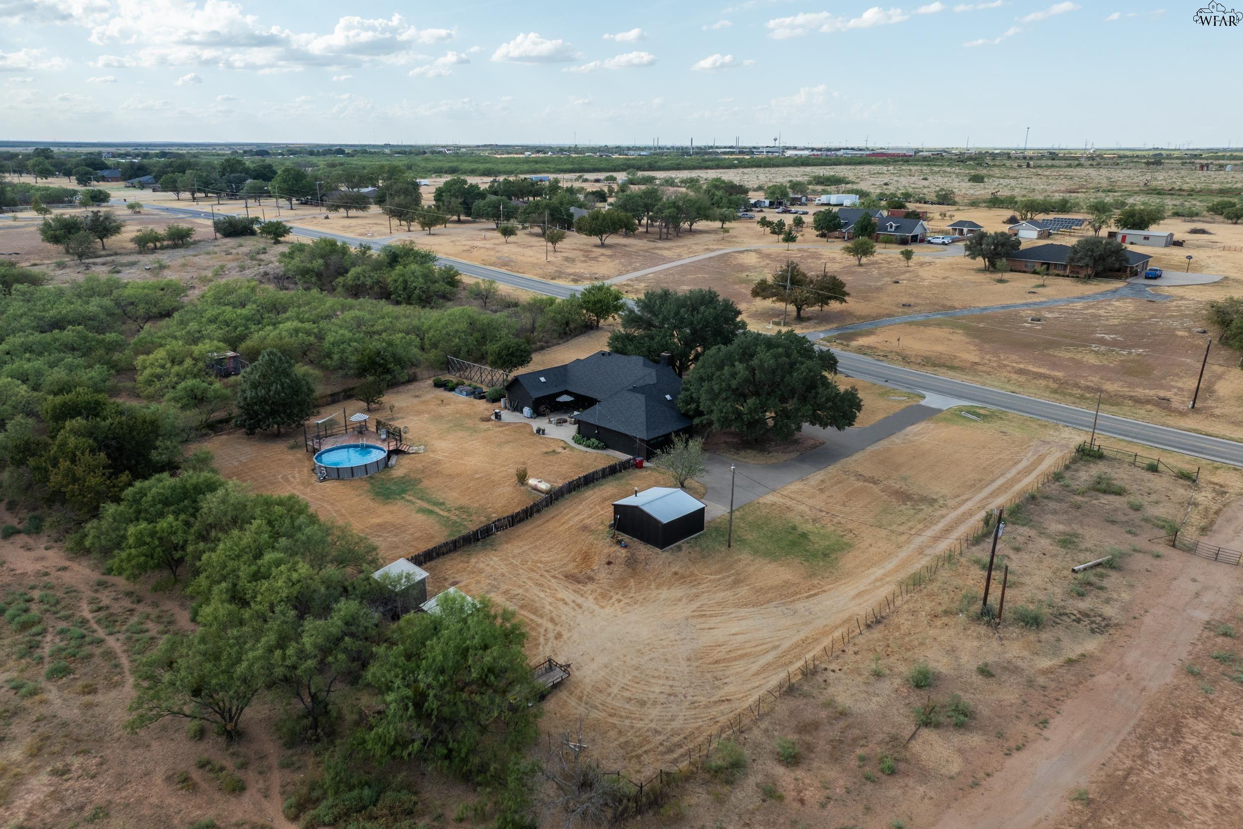 Aerial view of a rural home with a round above-ground pool, detached shed, and mature trees.