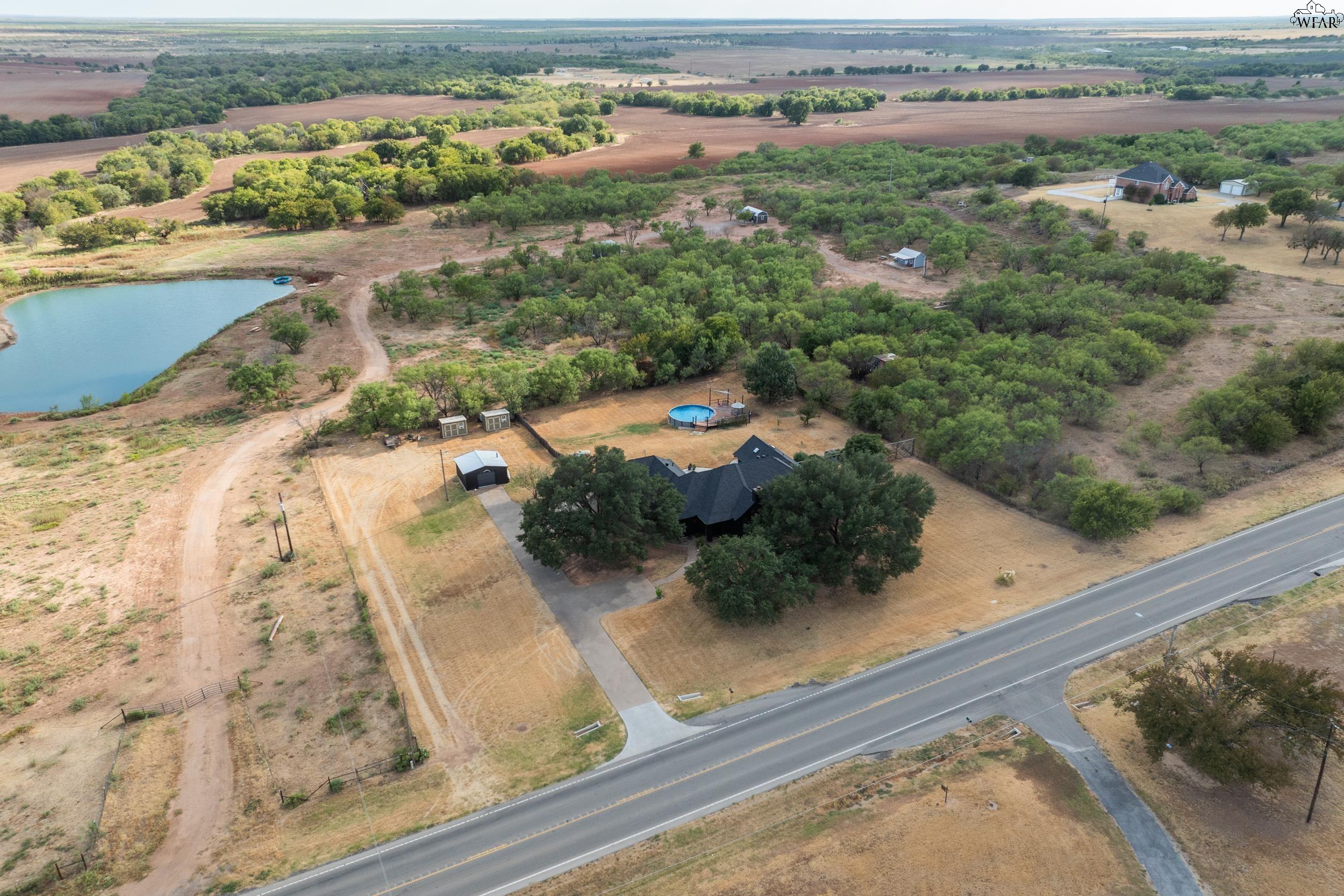 Aerial view of a rural home with a pool, pond, outbuildings, and surrounding acreage.