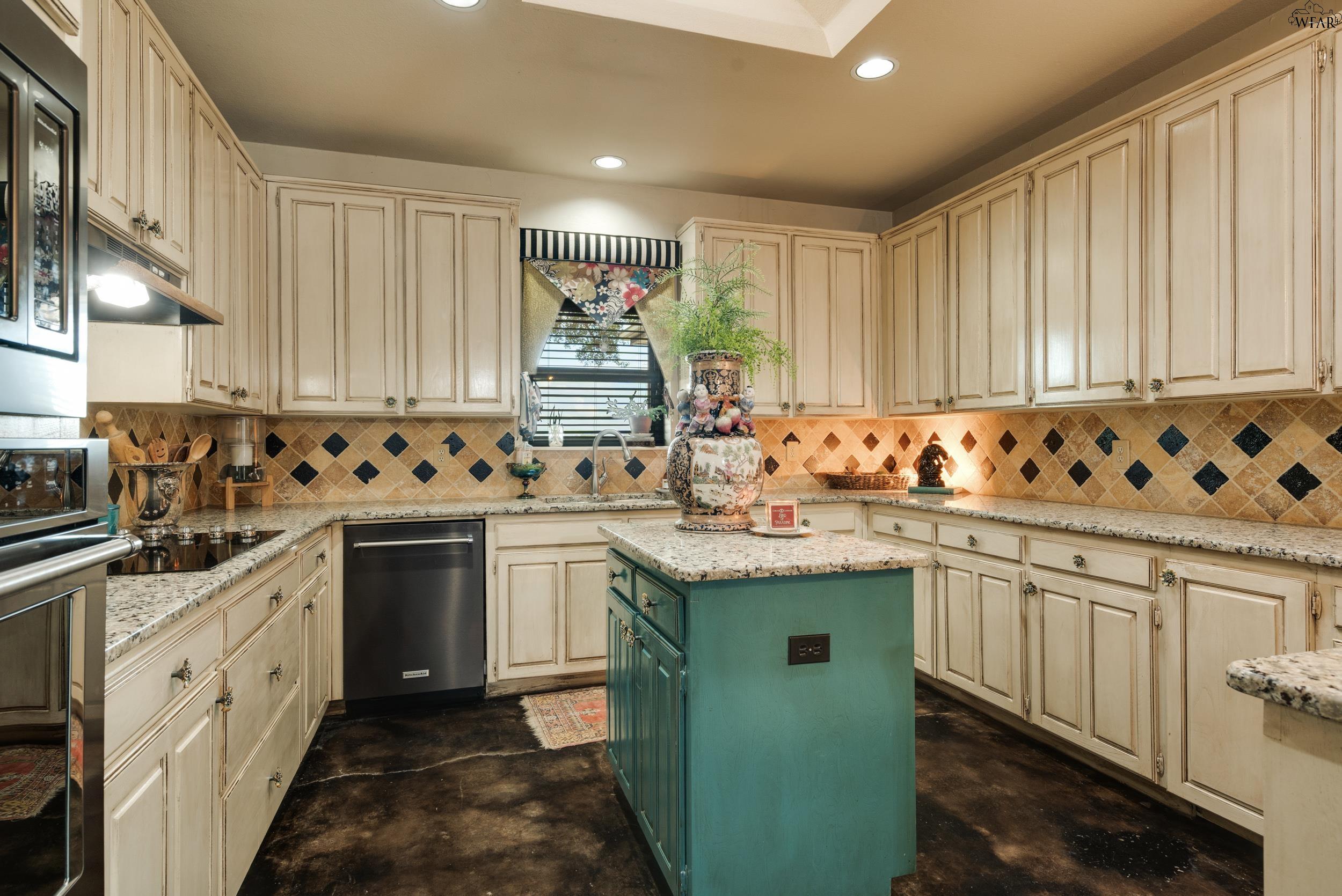 Kitchen with cream cabinets, granite counters, and a teal island topped with decorative pottery and a plant.