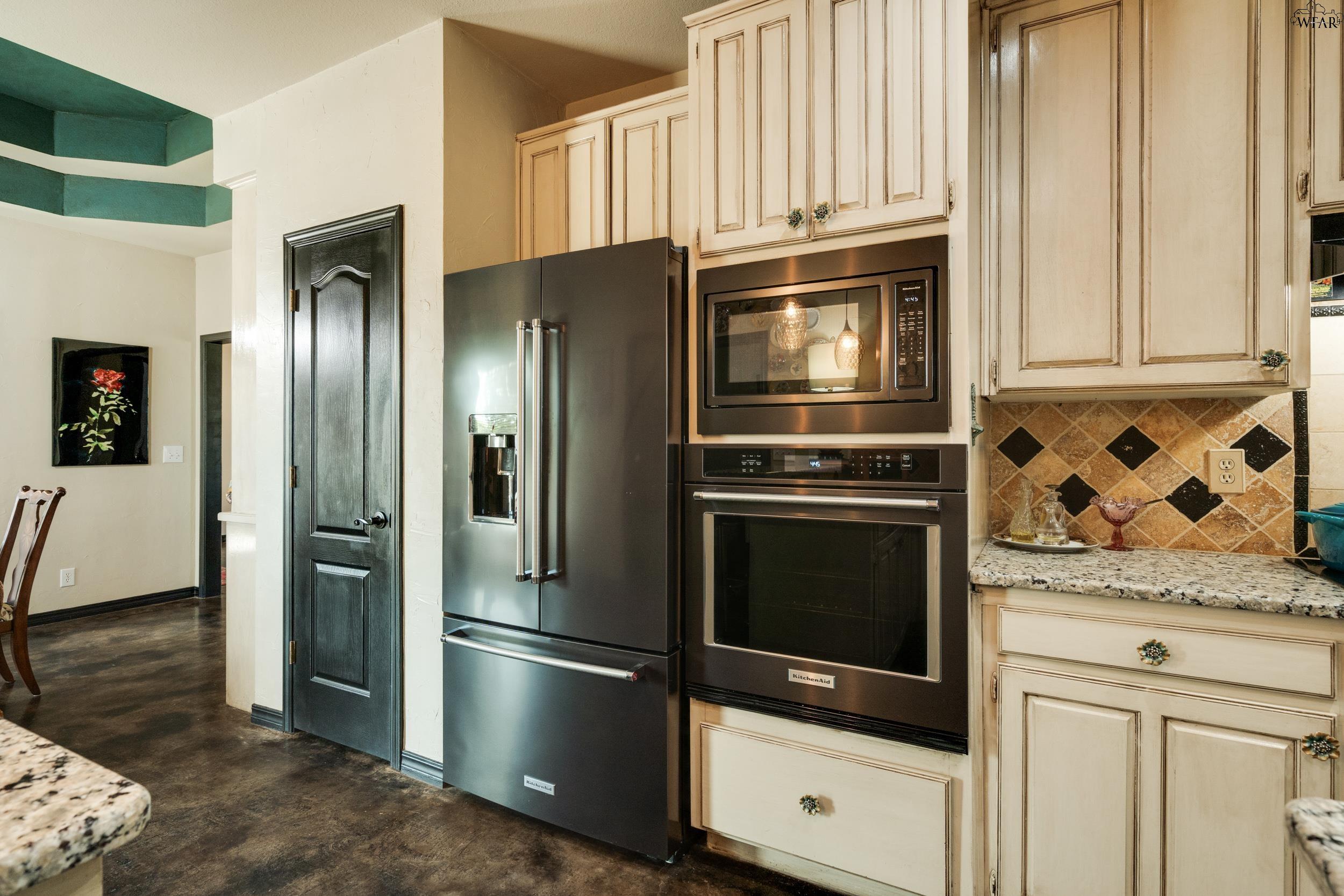 Kitchen with cream cabinets, stainless steel appliances, granite counters, and a tan diamond-pattern backsplash.