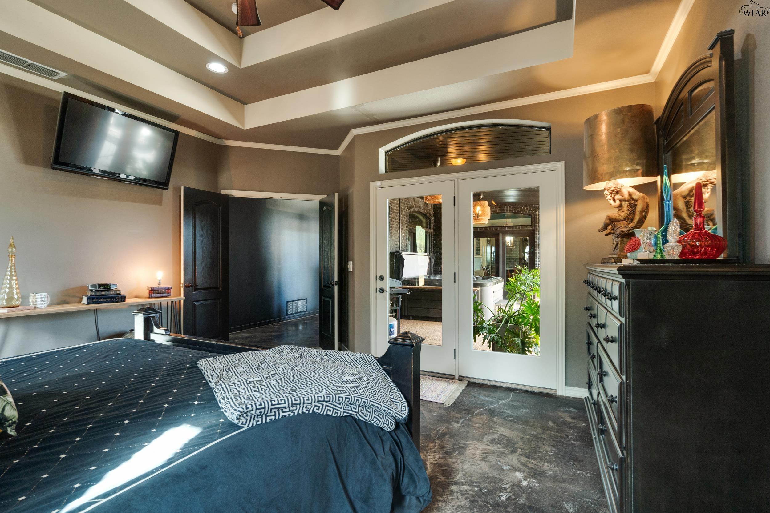 Furnished bedroom with French doors, a dark blue bed, and a tiered tray ceiling.