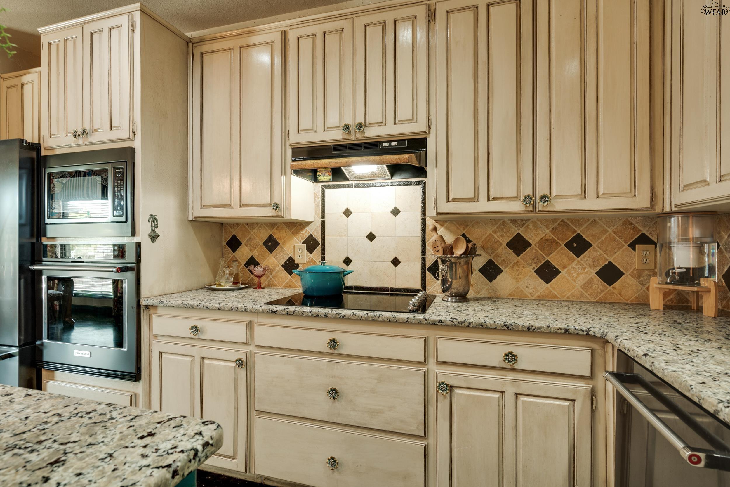 Kitchen with cream cabinets, granite counters, patterned tile backsplash, and built-in stainless steel appliances.