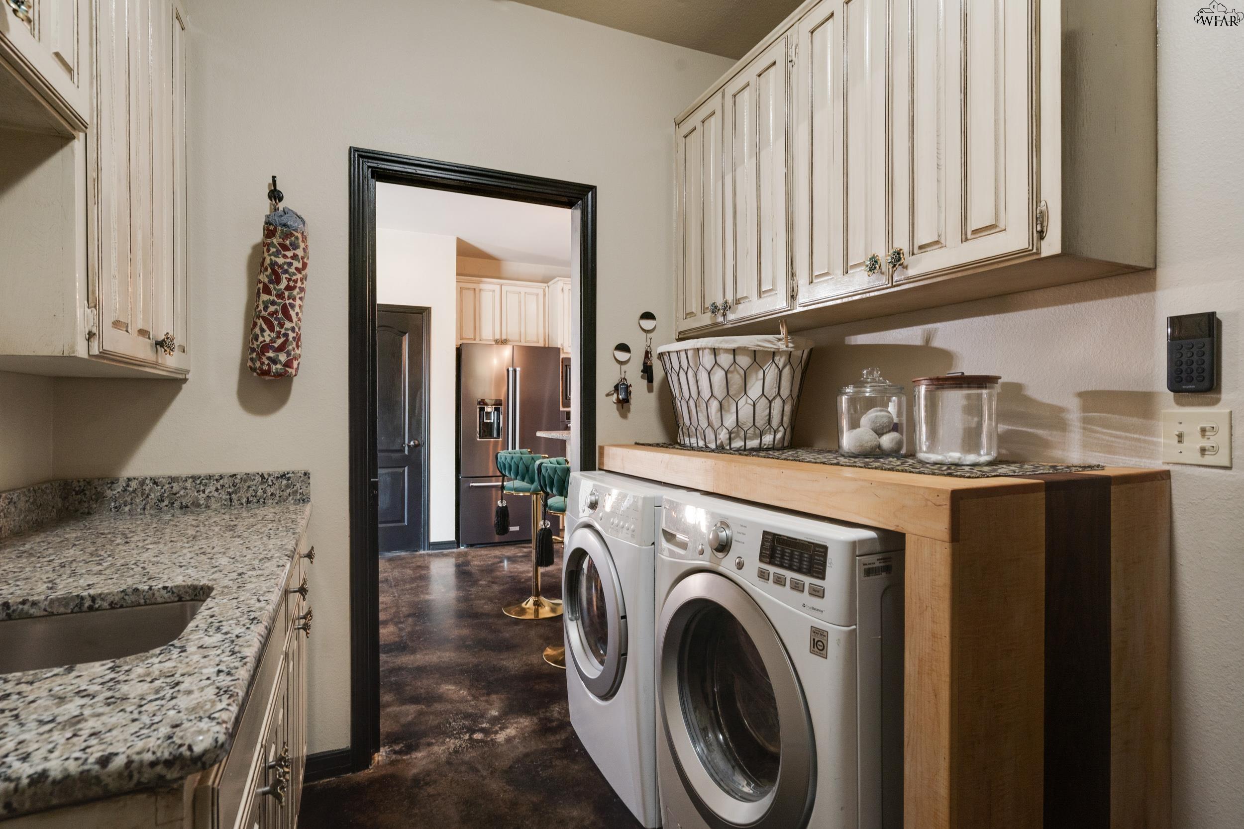 Laundry room with front-loading washer and dryer, wooden countertop, white cabinets, and granite utility sink.