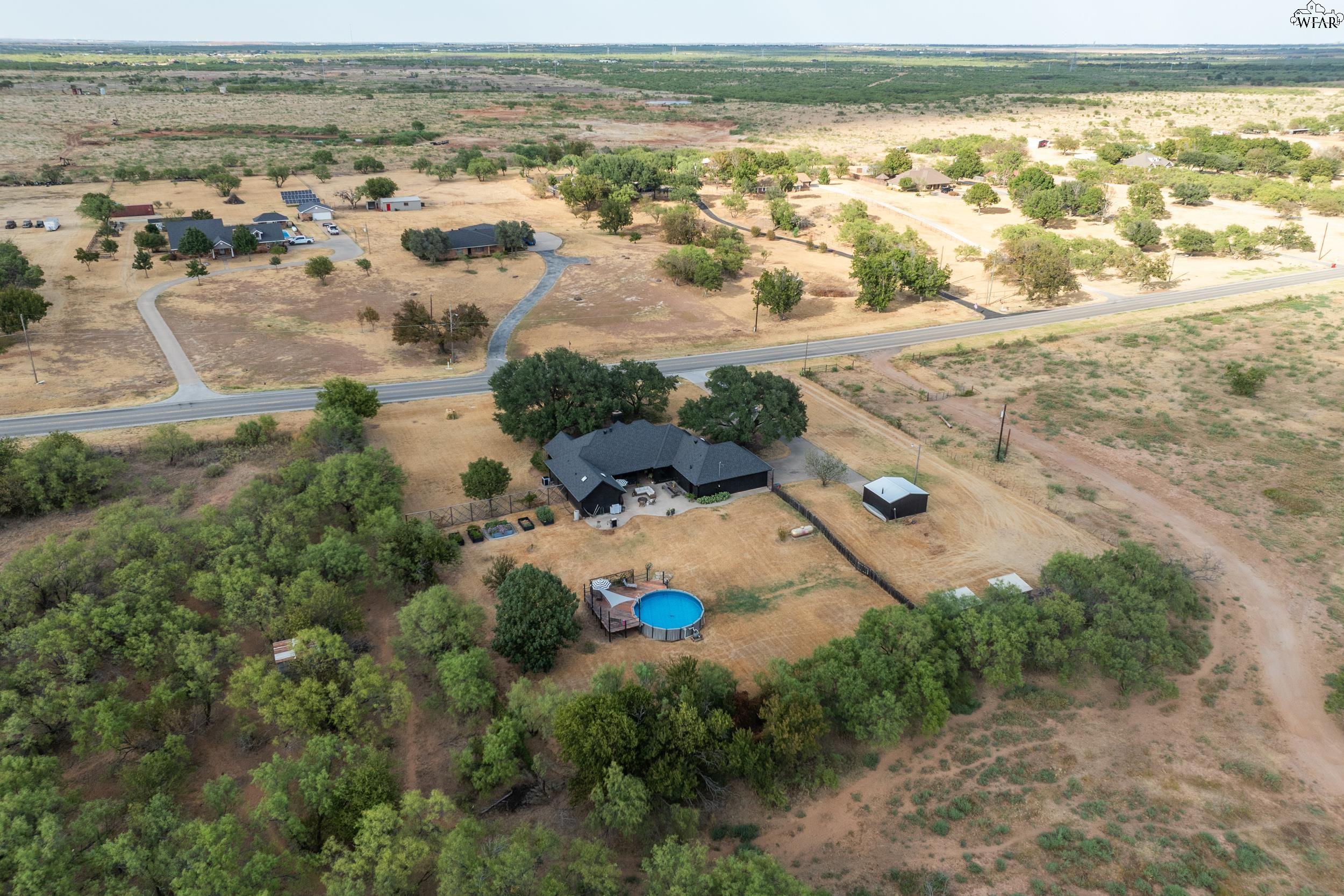 Aerial view of a rural home with an above-ground pool and detached outbuilding beside a paved road.