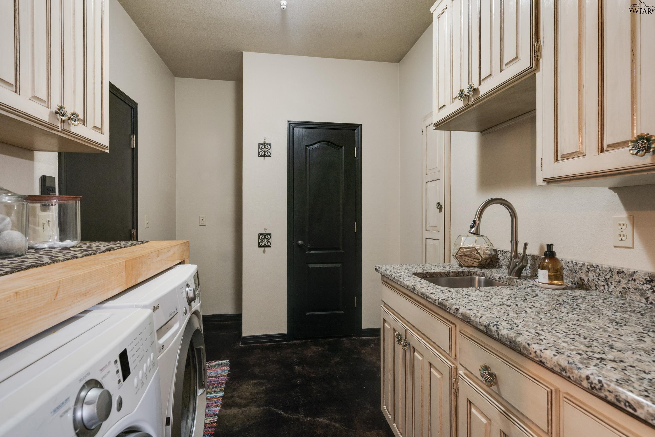 Laundry room with washer and dryer, cream cabinetry, granite counters, and a sink.