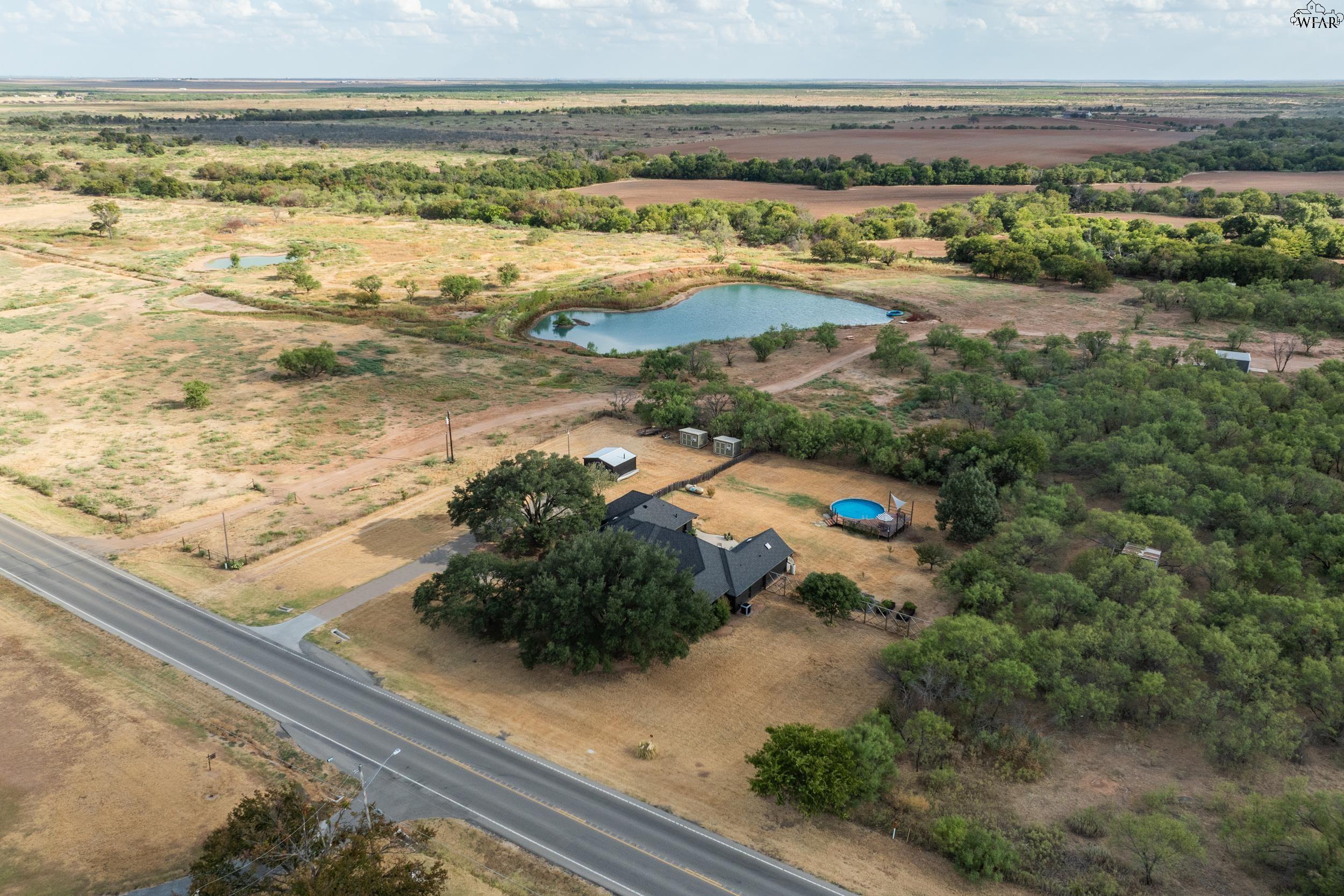 Aerial view of a rural home, pond, above-ground pool, outbuildings, and surrounding acreage.