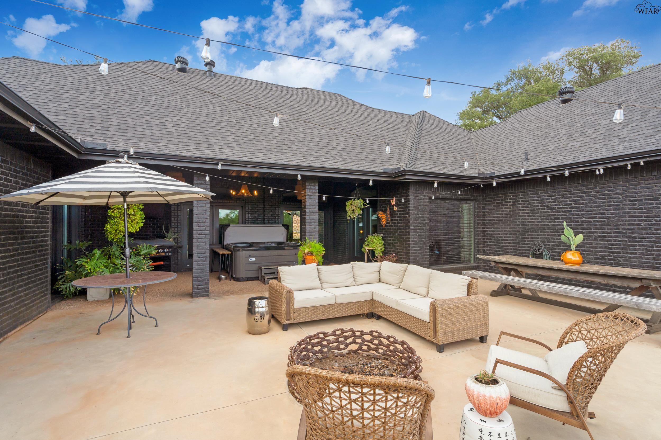 Covered brick patio with sectional seating, a hot tub, picnic table, and string lights.