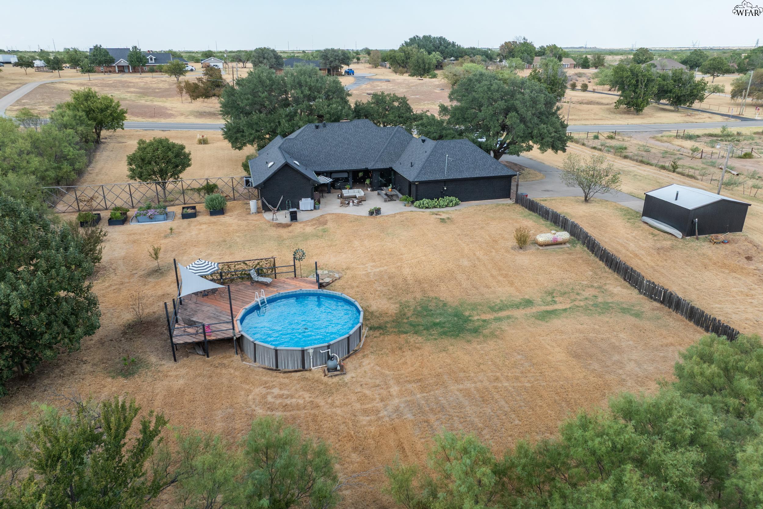 Aerial view of a dark brick home with a backyard pool, wooden deck, and detached shed.