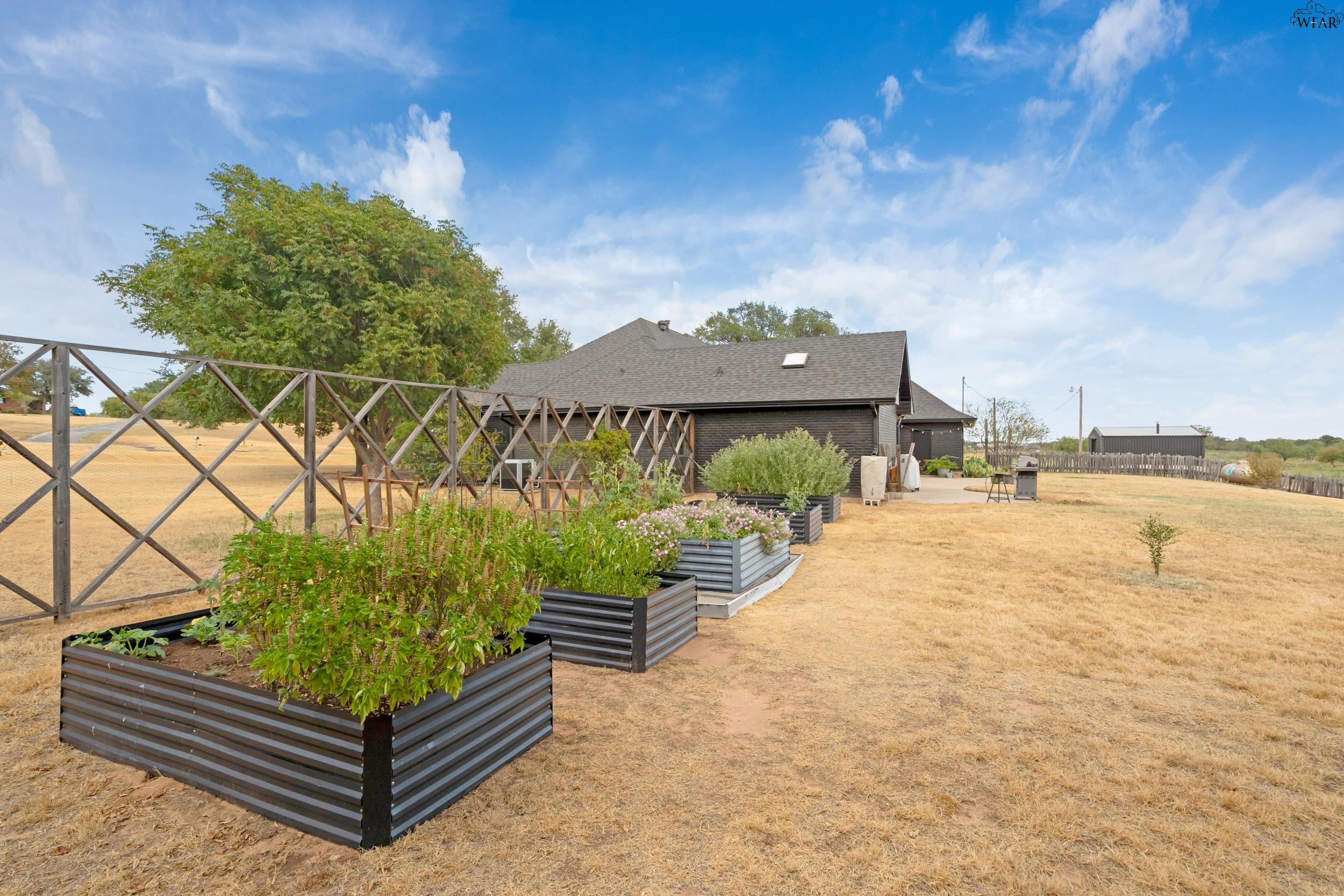 Rear of a dark-brick house with raised garden beds and a wooden trellis.