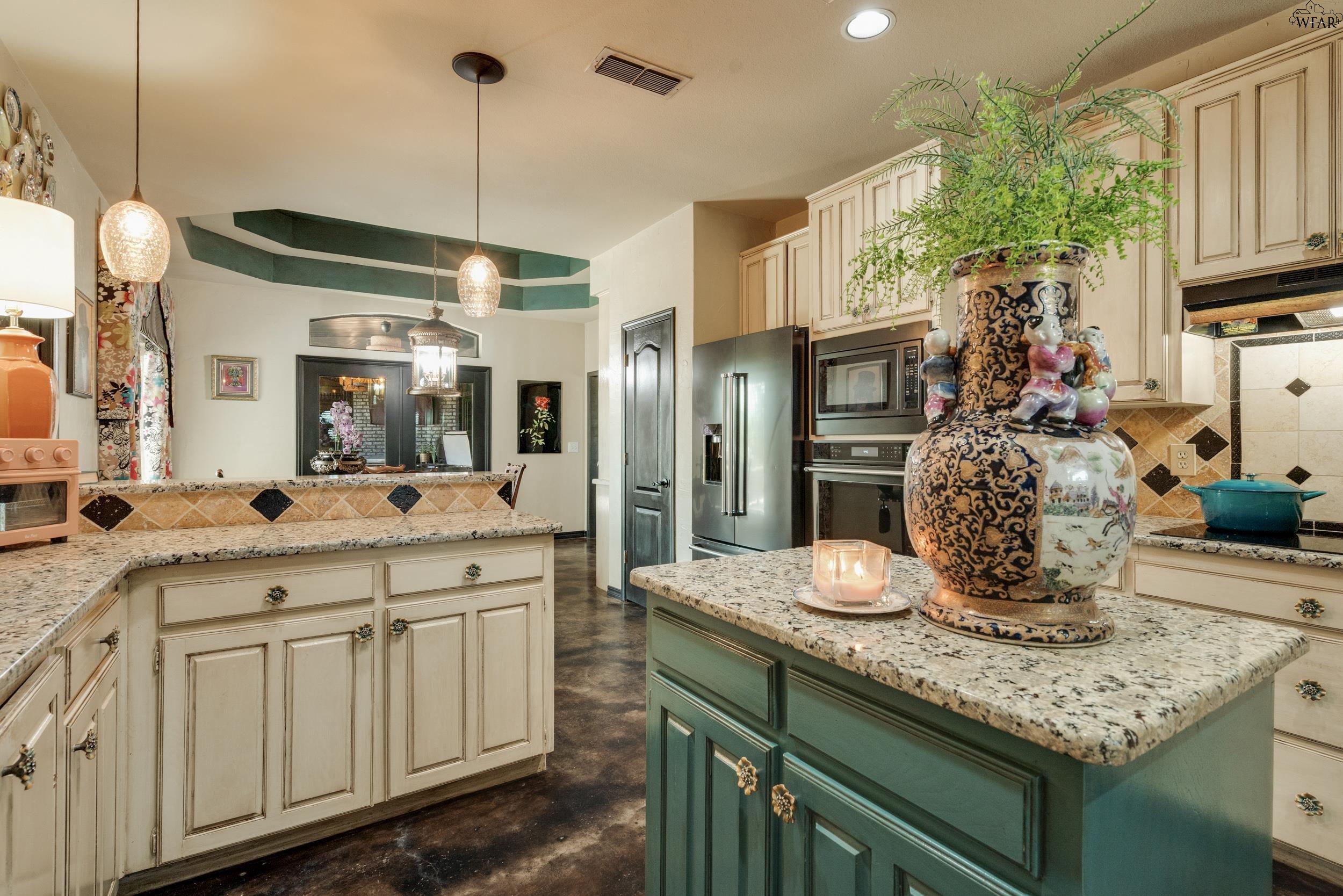 Kitchen with cream cabinetry, granite counters, and a green island topped by a large vase and fern.