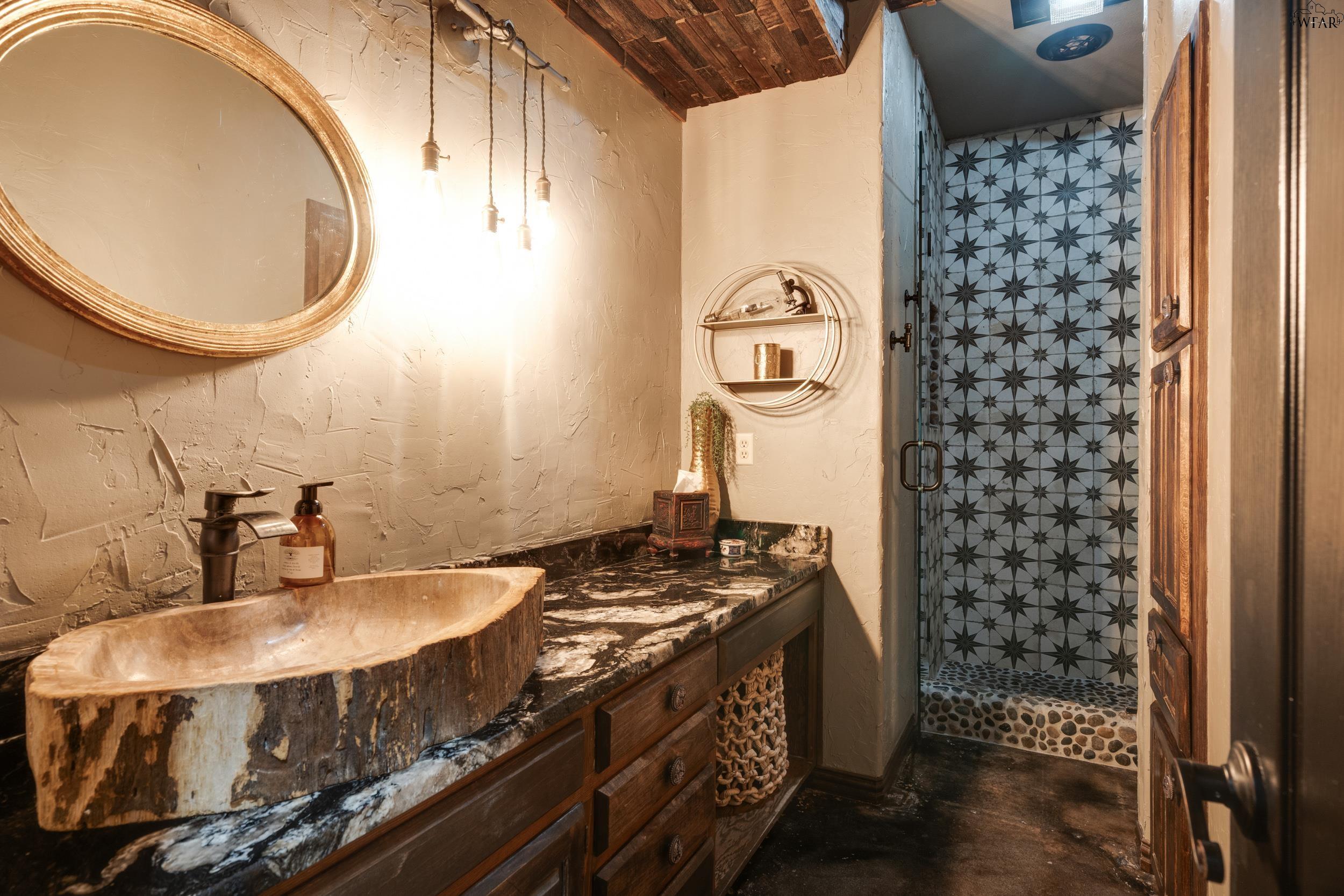 Rustic bathroom with a stone vessel sink and a geometric tile walk-in shower.