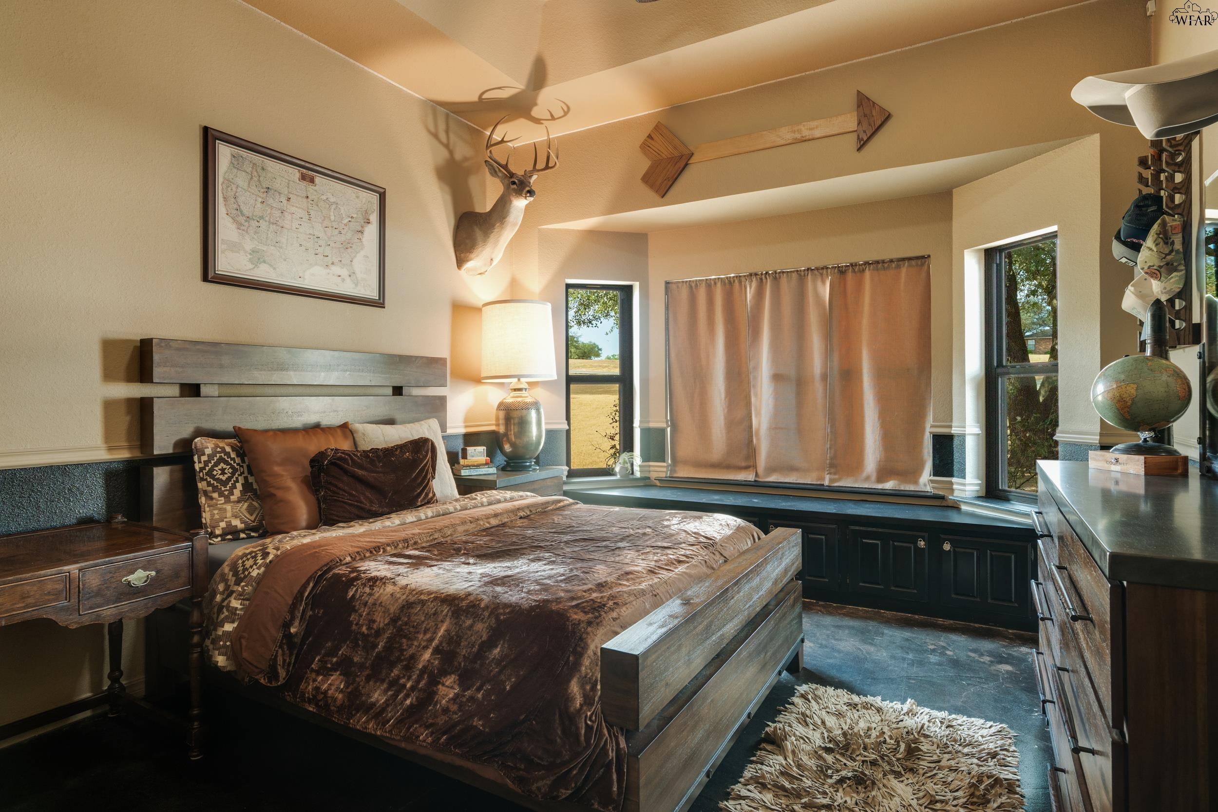 Bedroom with rustic dark wood furniture, brown bedding, a mounted deer head, and tall windows.