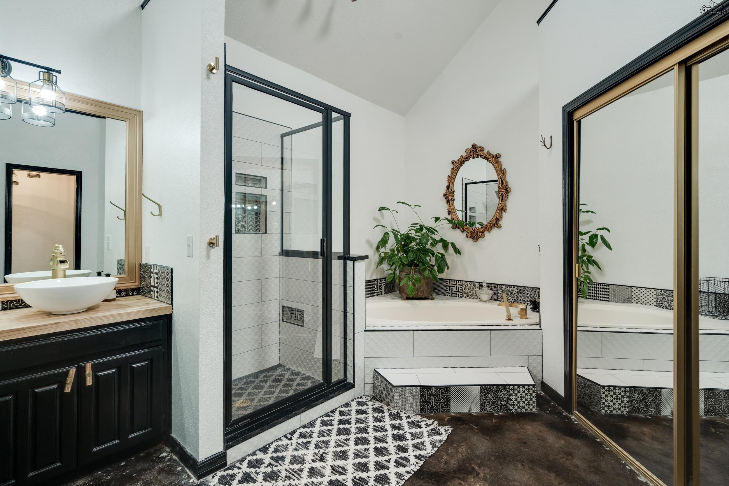 Bathroom with glass shower, built-in soaking tub, black vanity, and patterned tile accents.