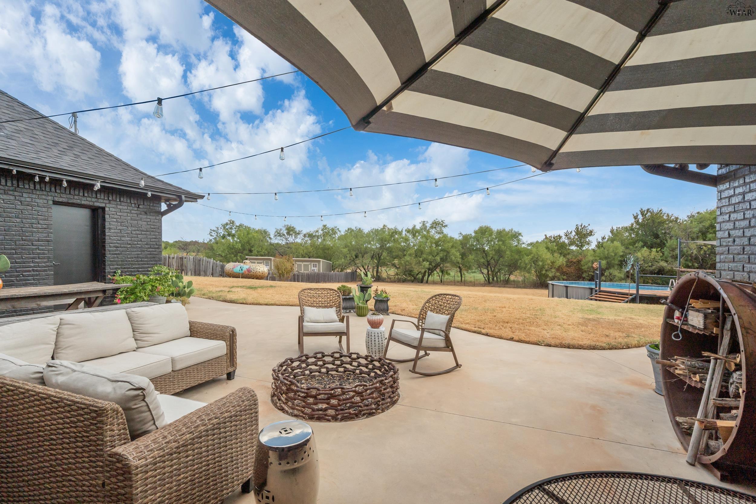 Furnished patio with wicker seating, striped umbrella, string lights, and an above-ground pool.