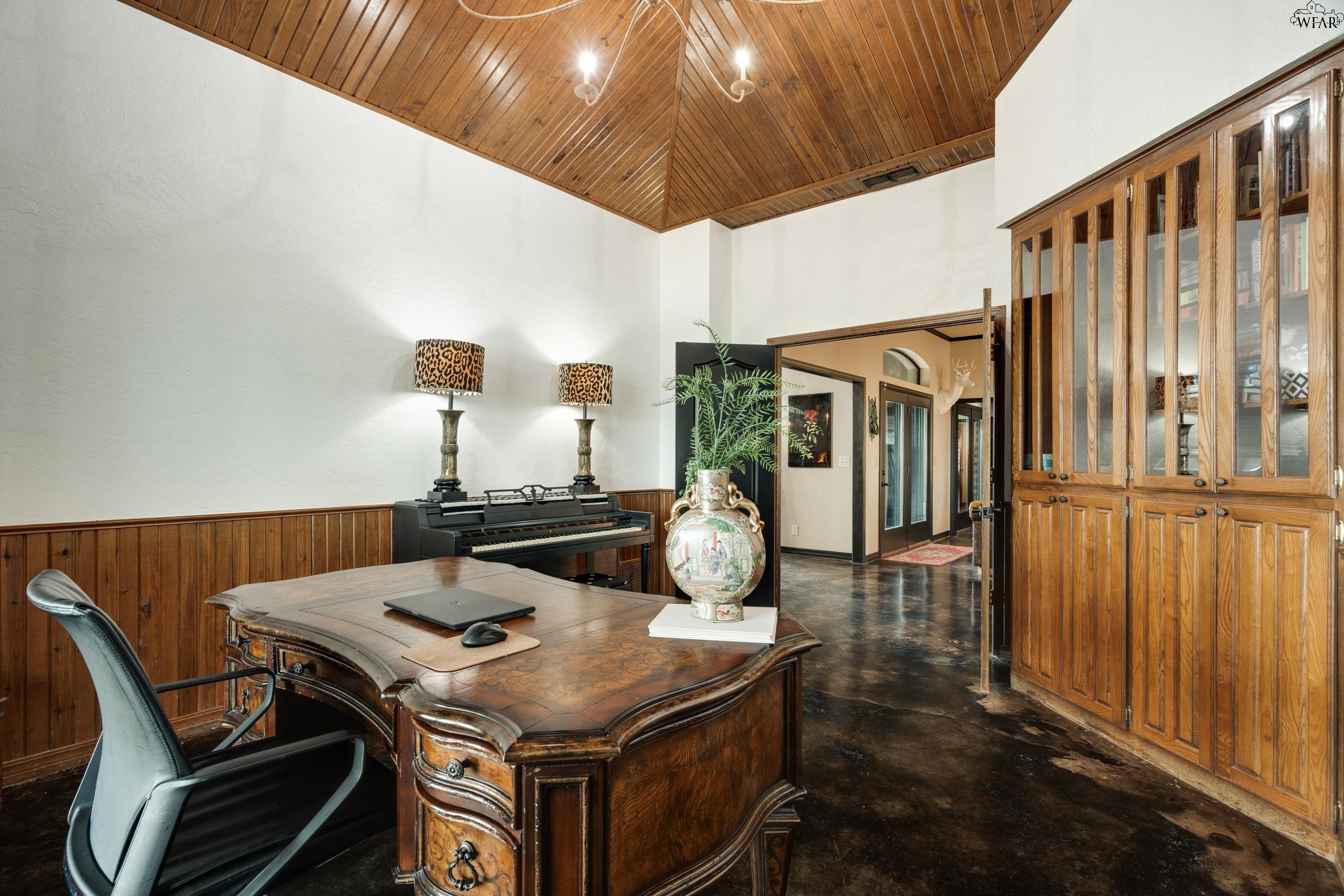 Home office with a vaulted wood ceiling, ornate desk, piano, and glass-front cabinet.
