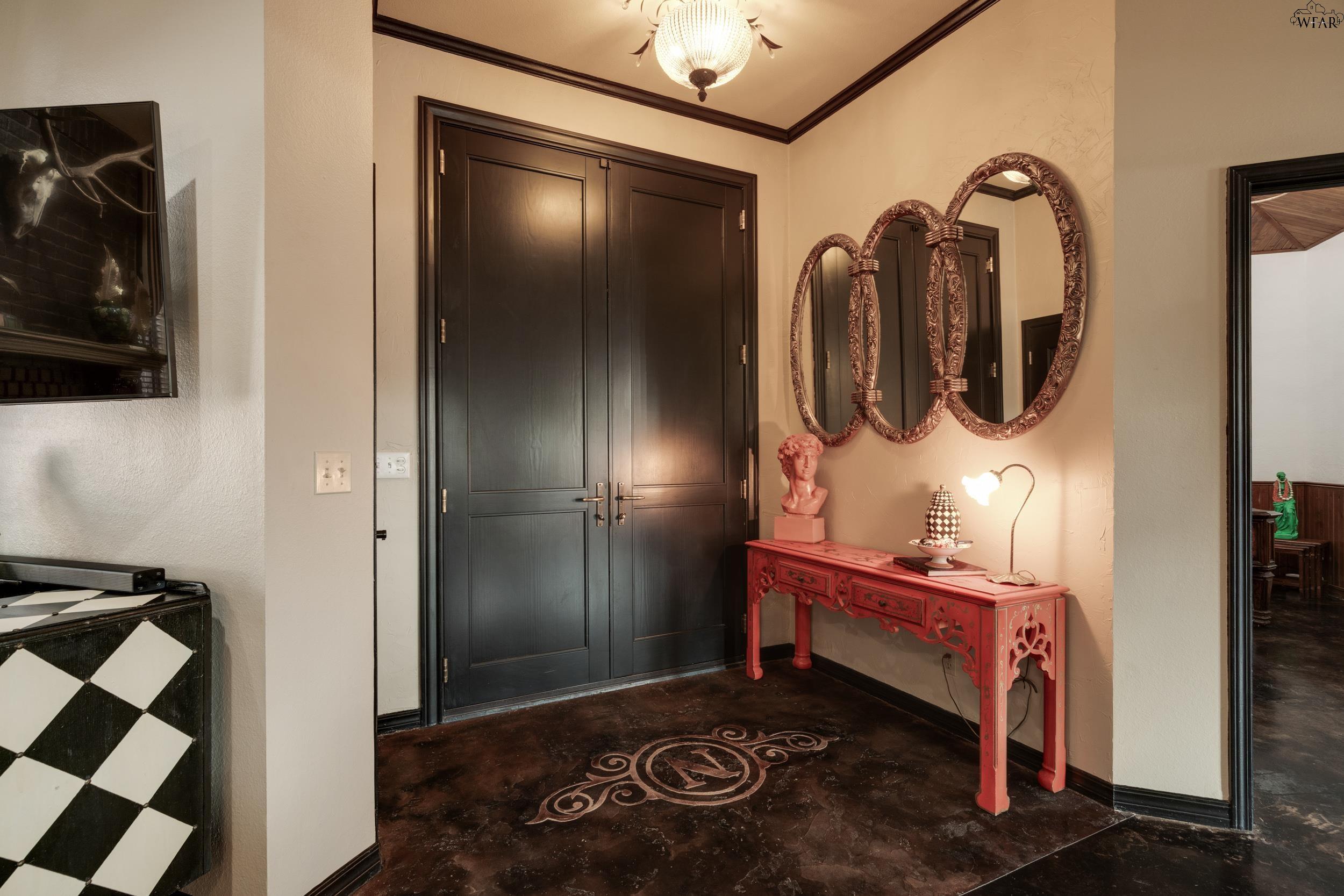 Entry foyer with dark double doors, a red carved console table, and three ornate oval mirrors.