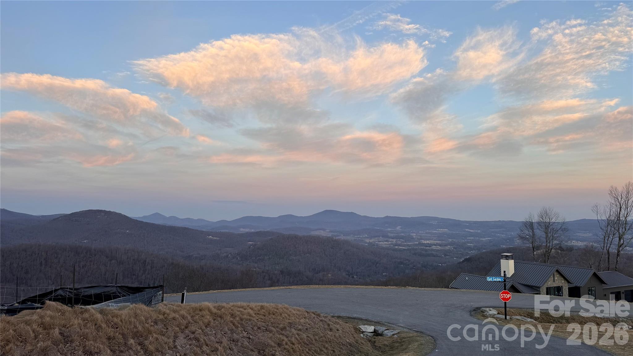 Mountain-view homesite overlooking wooded ridges, with a neighborhood road and building at dusk.