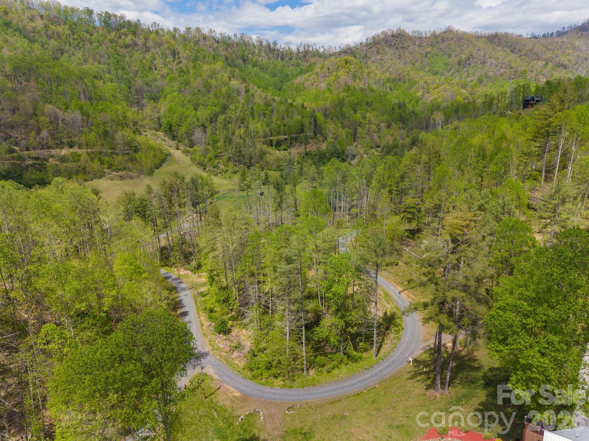 Aerial view of wooded mountain land with a winding gravel road and grassy clearing.