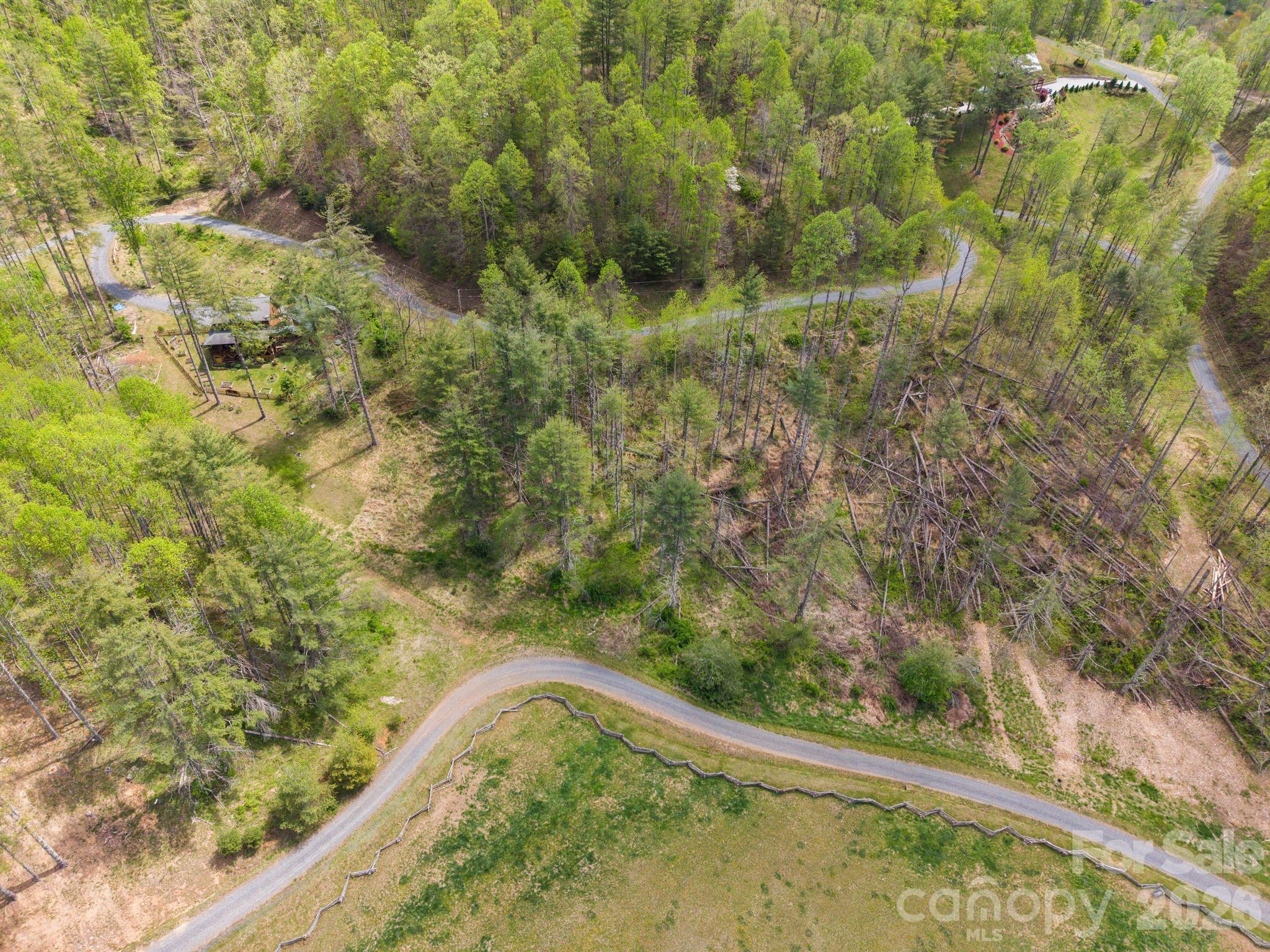 Aerial view of wooded land with winding gravel roads, a fenced clearing, and a small cabin.