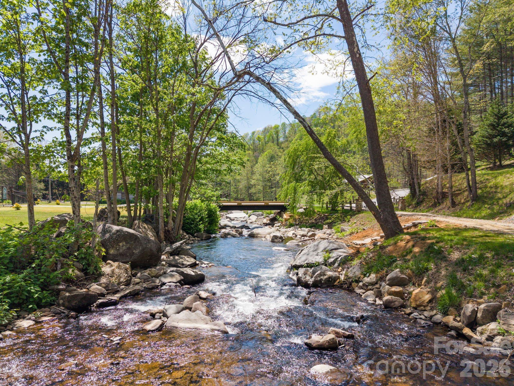 Rocky creek flows beneath a small bridge through a wooded property.