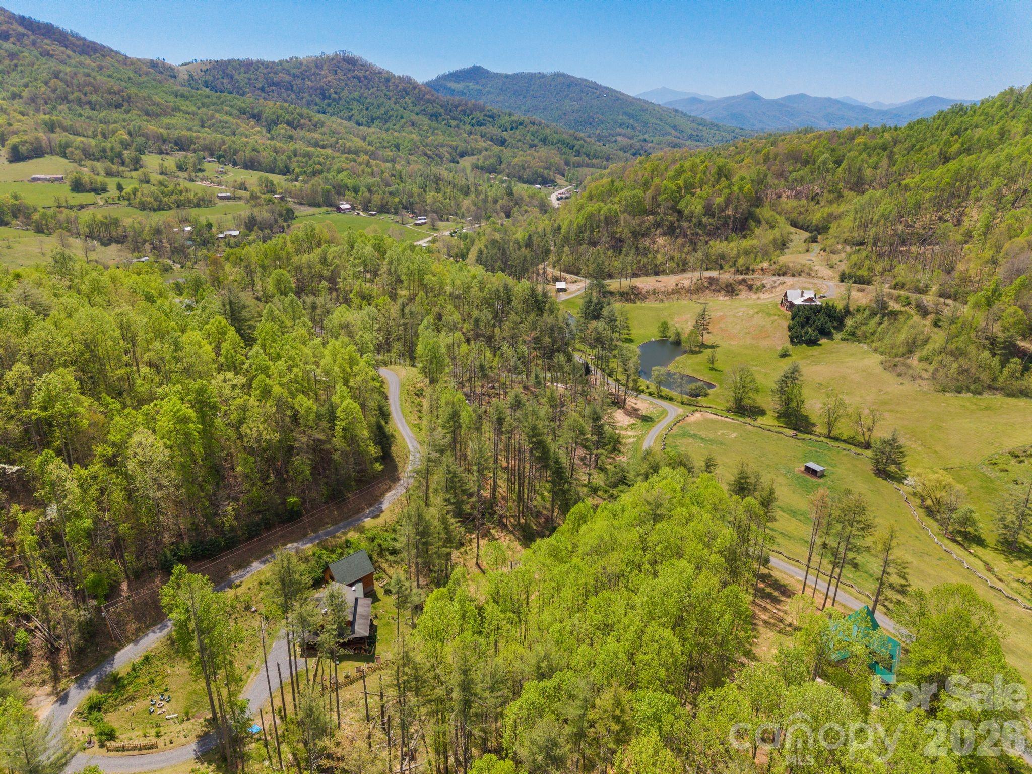 Aerial view of a wooded mountain property with open fields, winding roads, and a small pond.