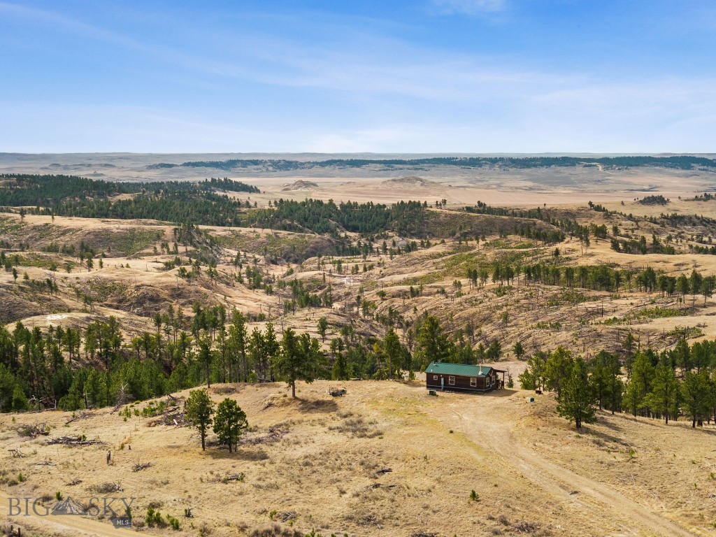 Aerial view of a small cabin amid rolling, sparsely wooded grassland and distant open plains.