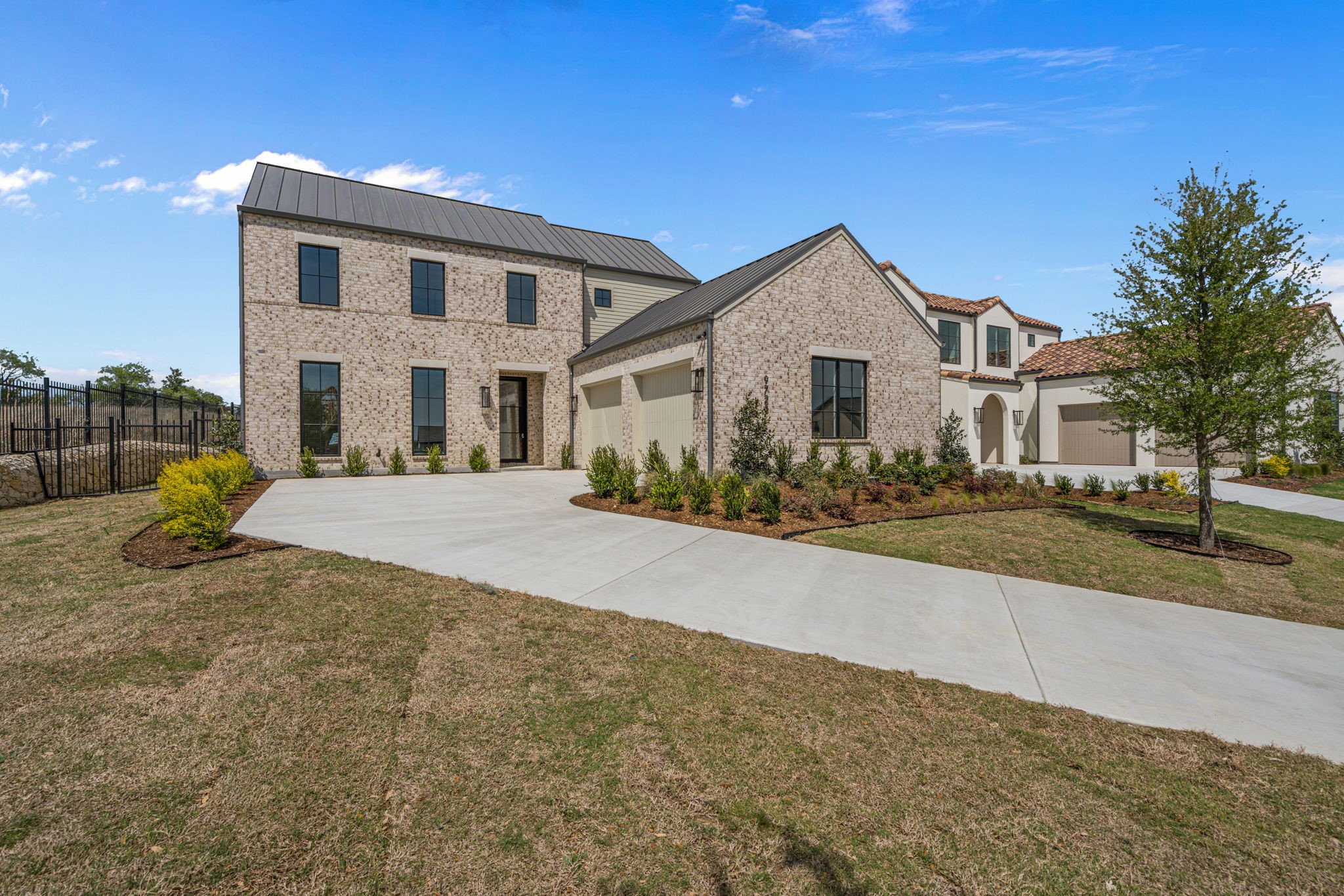 Two-story brick home with dark metal roofs, an attached garage, and a broad concrete driveway.