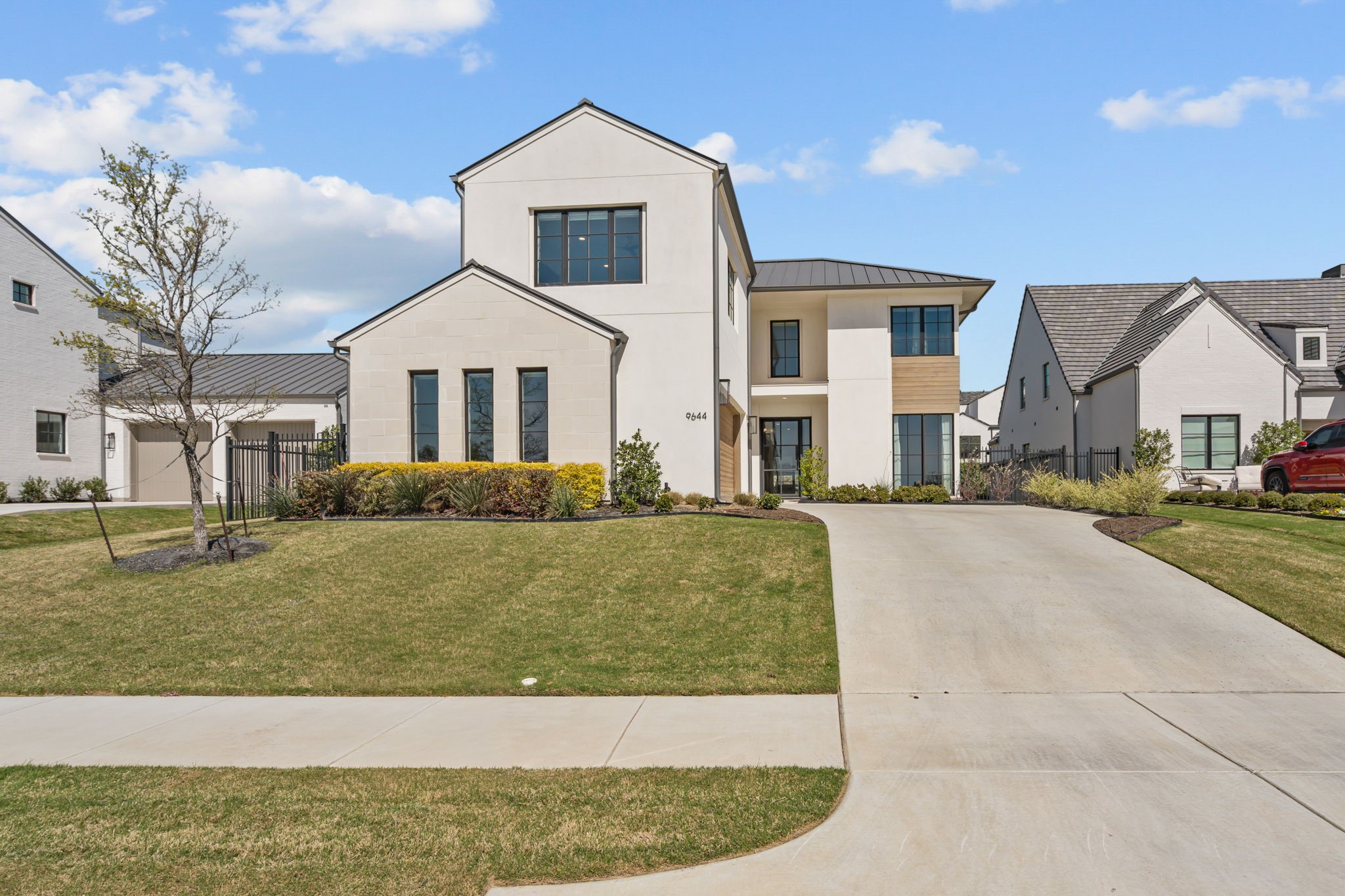 Modern two-story white home with dark-framed windows, landscaped beds, and a broad curved driveway.