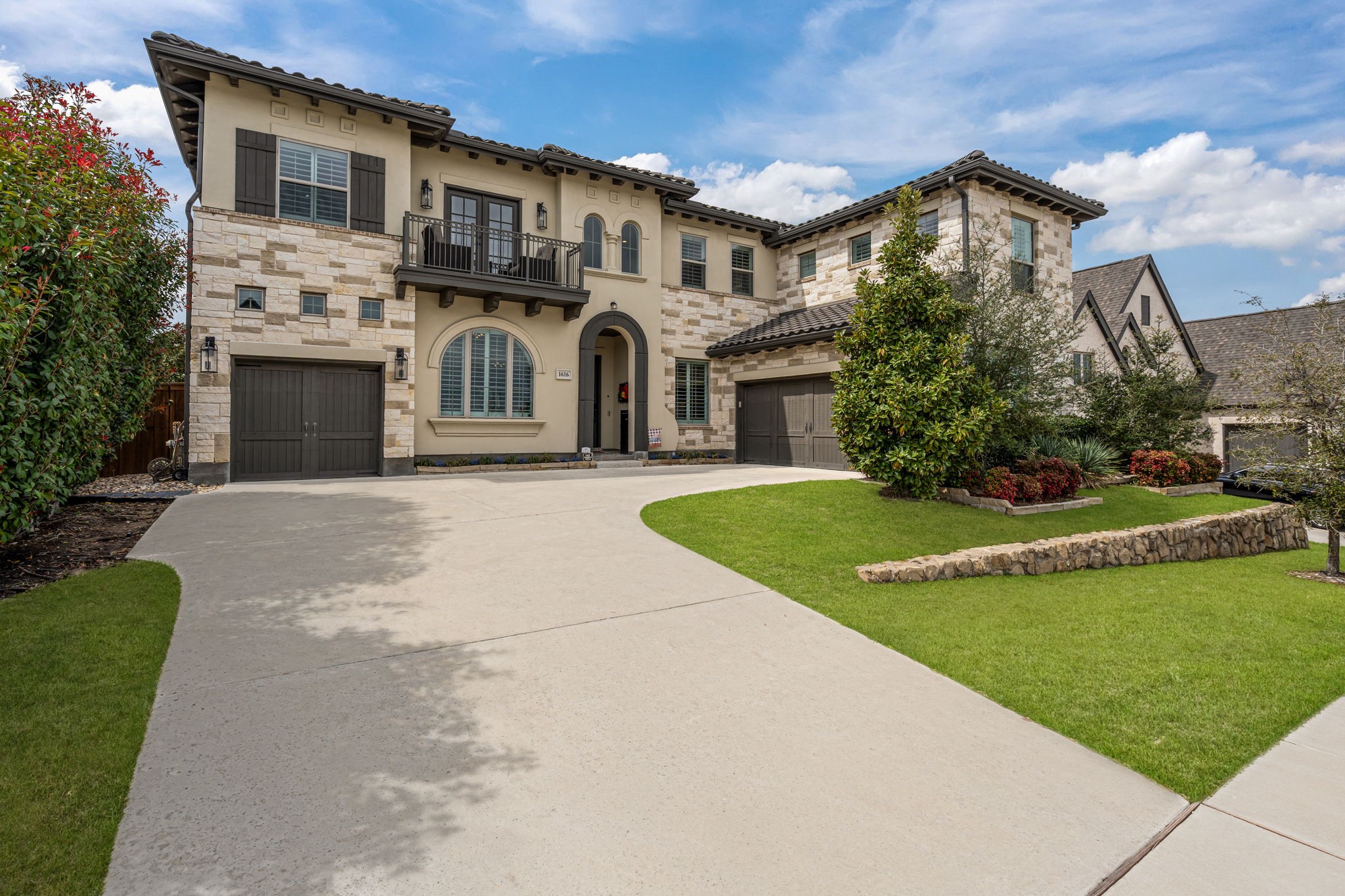 Two-story stone-and-stucco home with two garages, a balcony, and a landscaped front lawn.