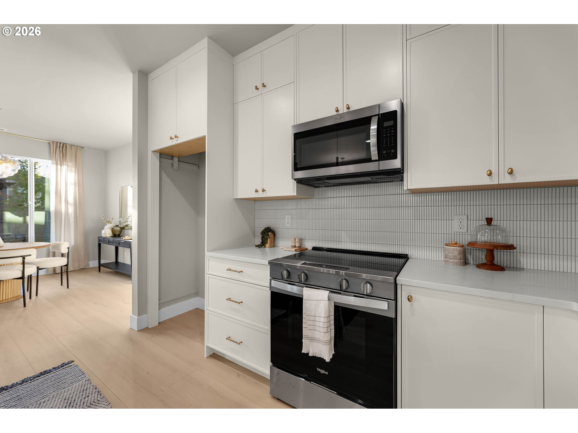 Bright white kitchen with brass cabinet pulls, gray tile backsplash, and stainless steel appliances.