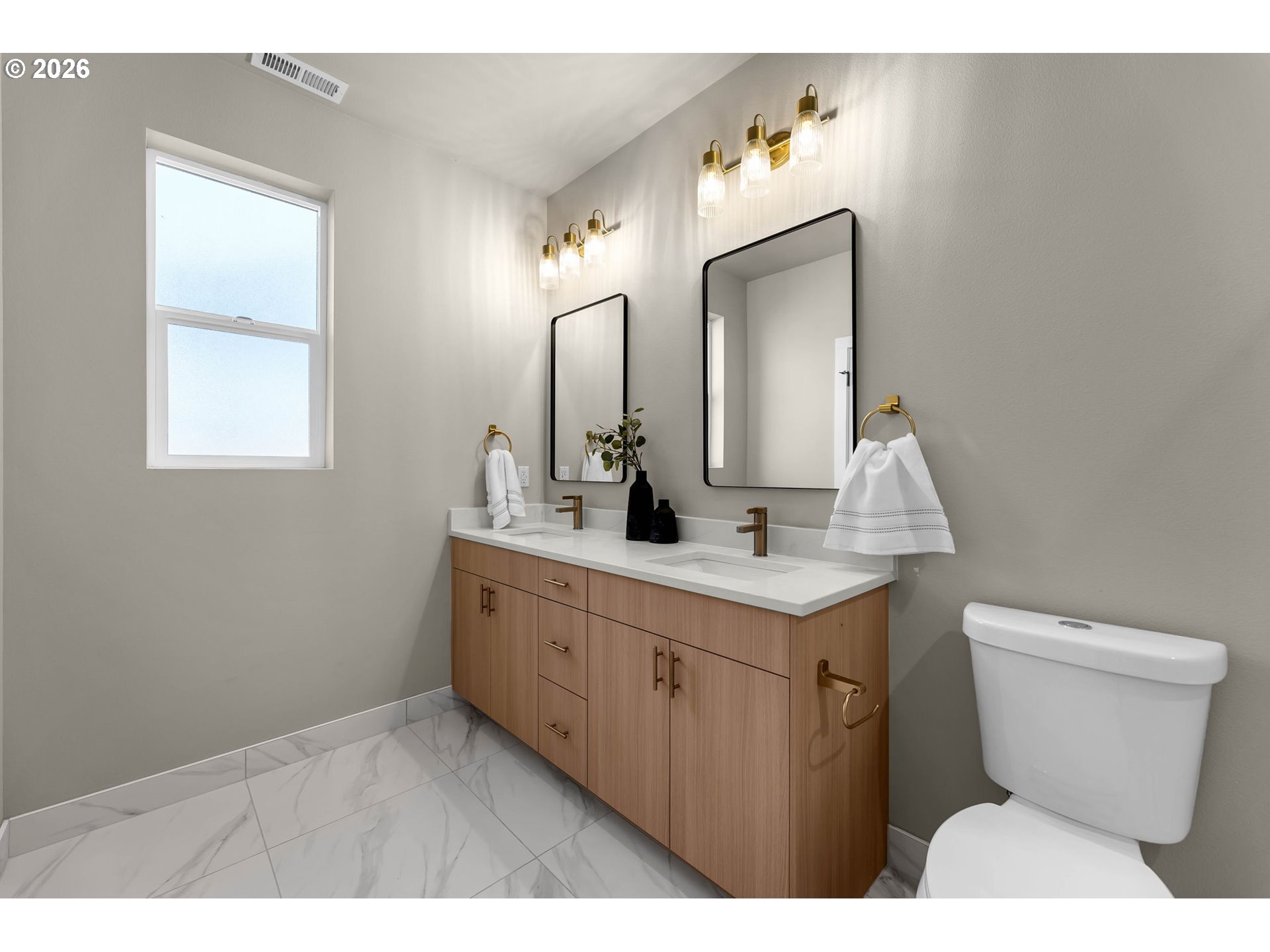 Bathroom with a wood double vanity, two black-framed mirrors, marble-look tile, and brass lighting.