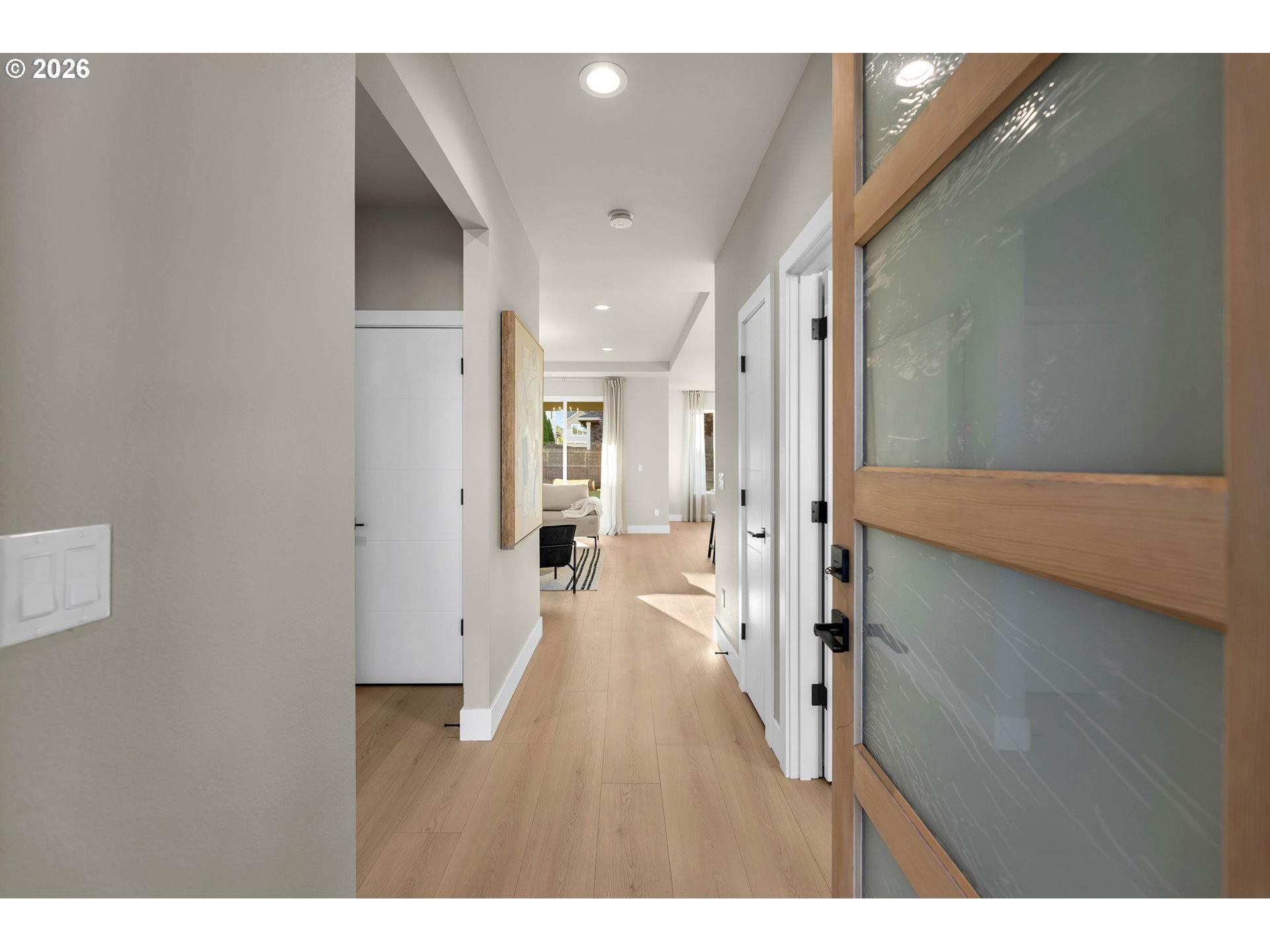 Entry hallway with light wood floors, recessed lights, and an open view into the living area.