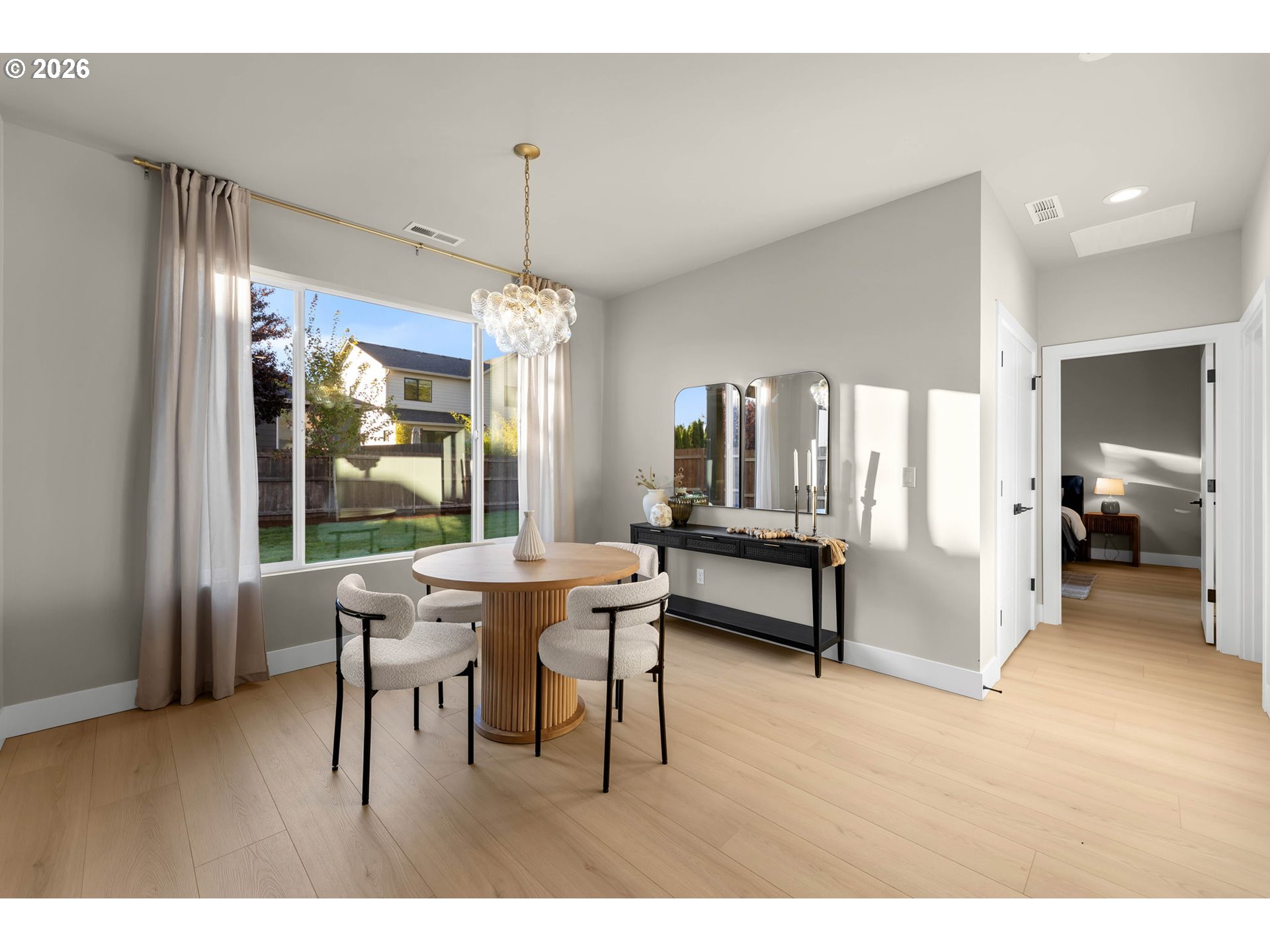 Dining area with a round table and upholstered chairs beside a large window overlooking the backyard.