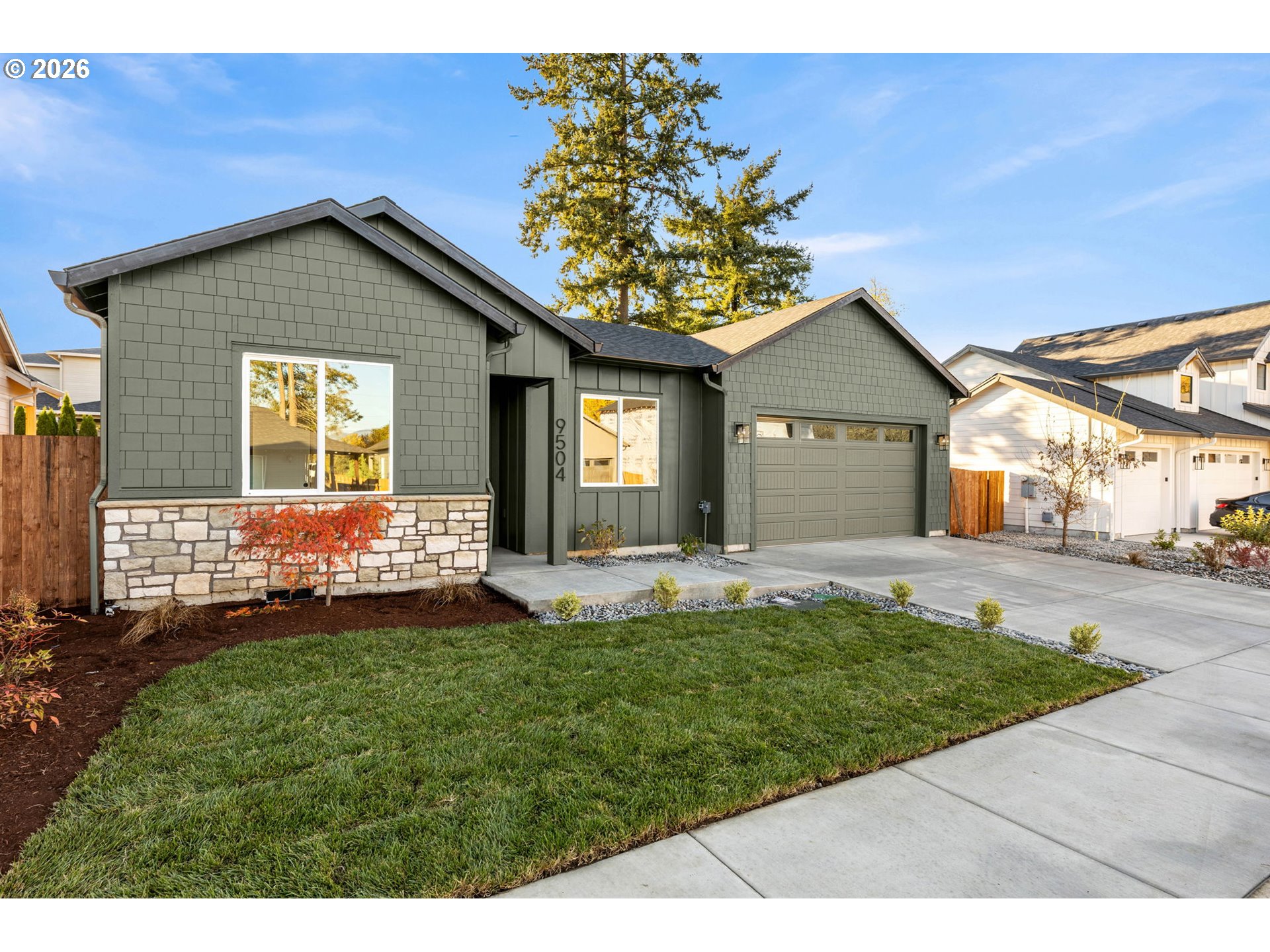 Gray-green single-story home with a stone-accented facade, two-car garage, and landscaped front lawn.
