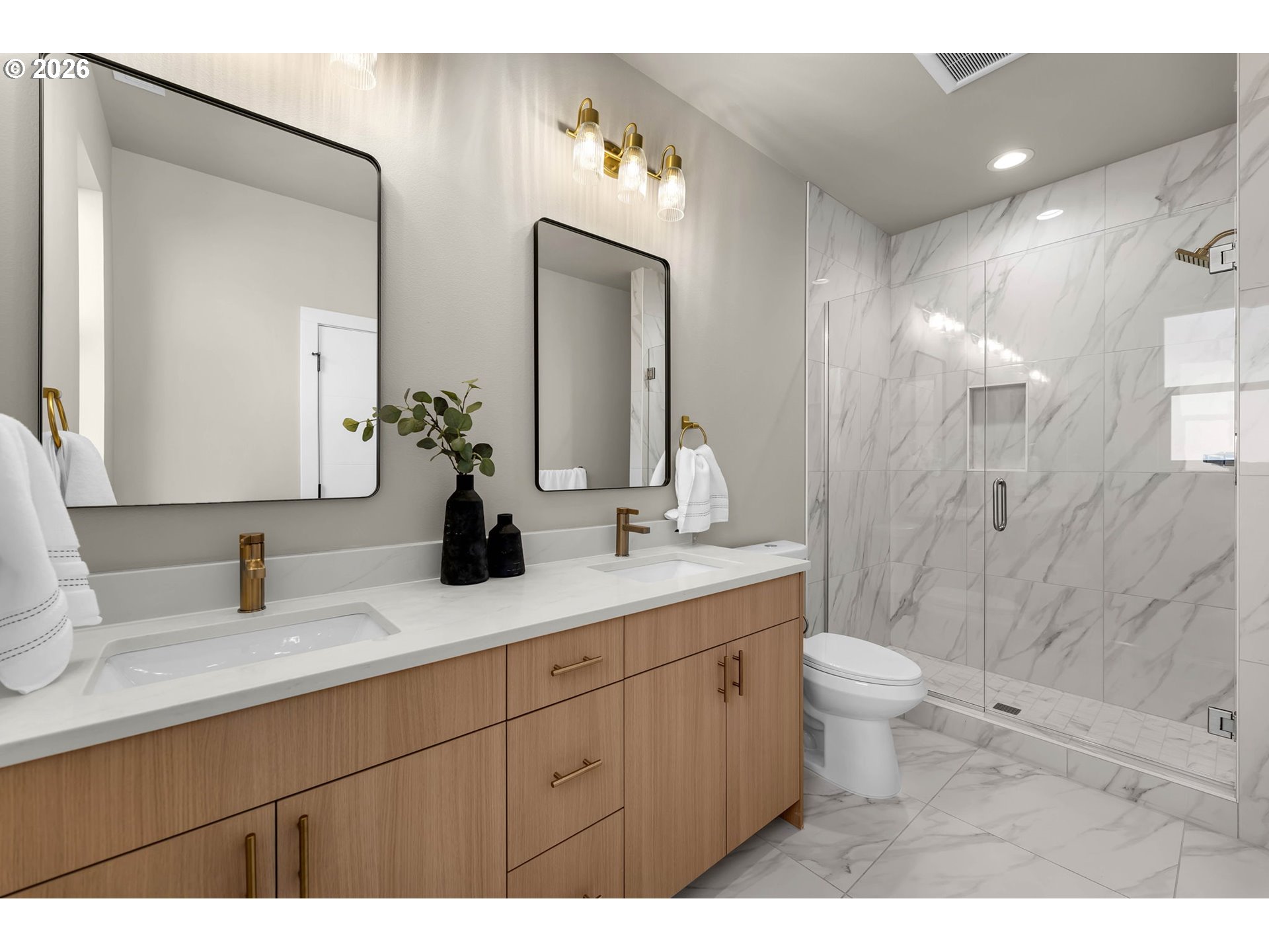 Modern bathroom with a light wood double vanity and glass-enclosed marble-look shower.