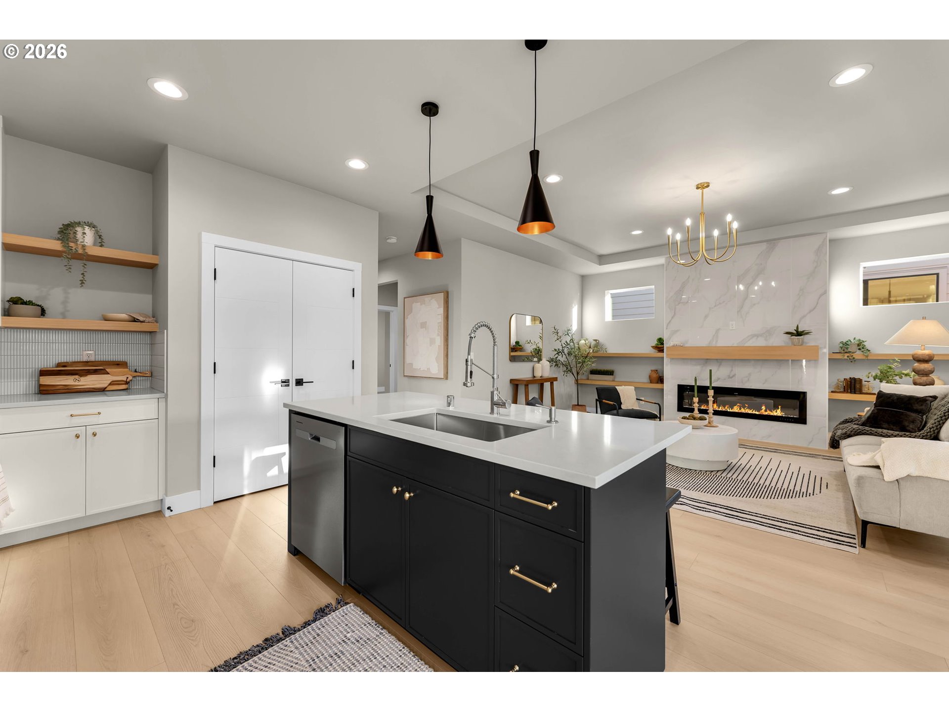 Open-plan kitchen with a black island and white counters facing a living room with a marble fireplace.