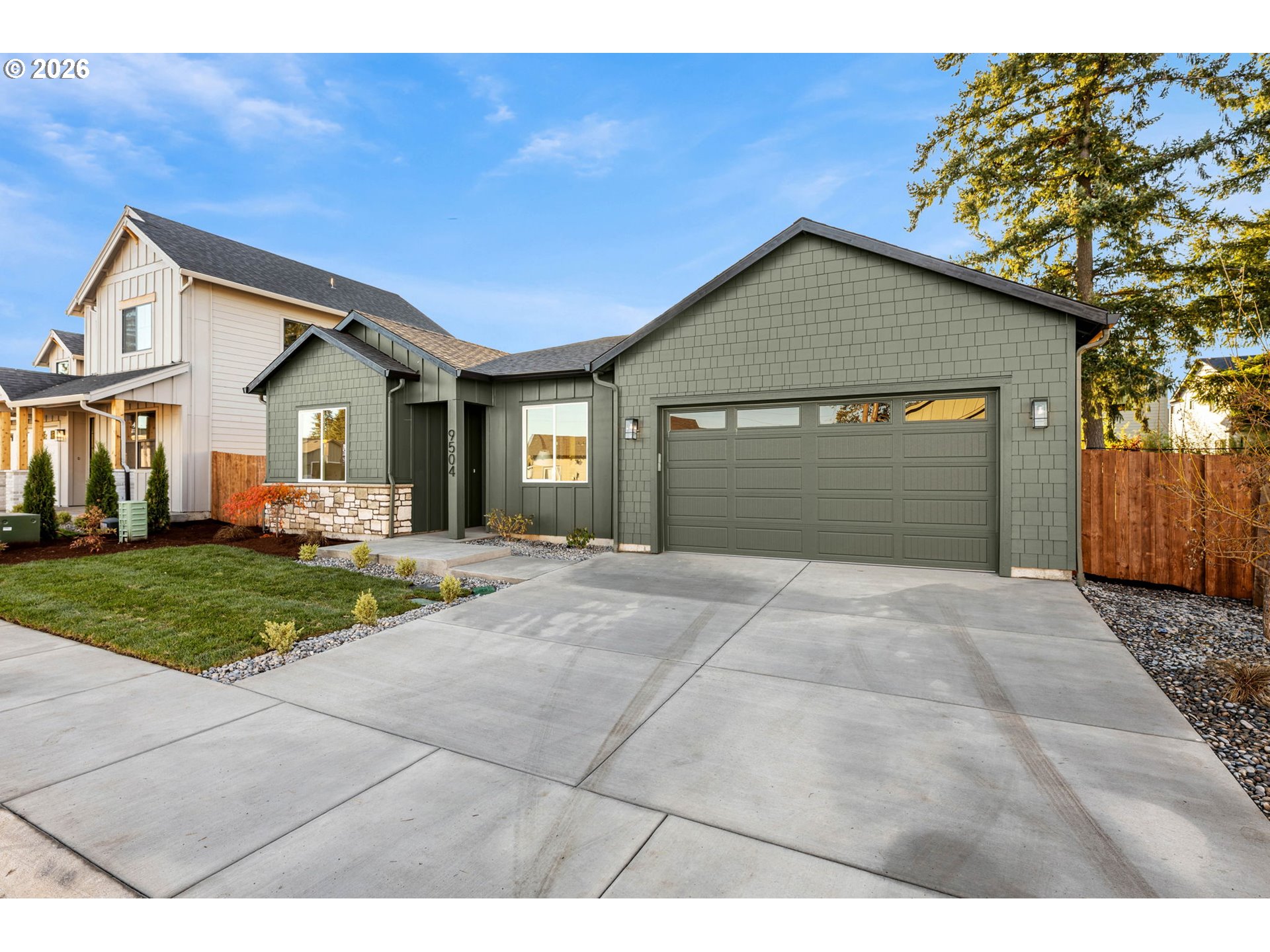 Gray-green home with stone accents, a two-car garage, and a broad concrete driveway.