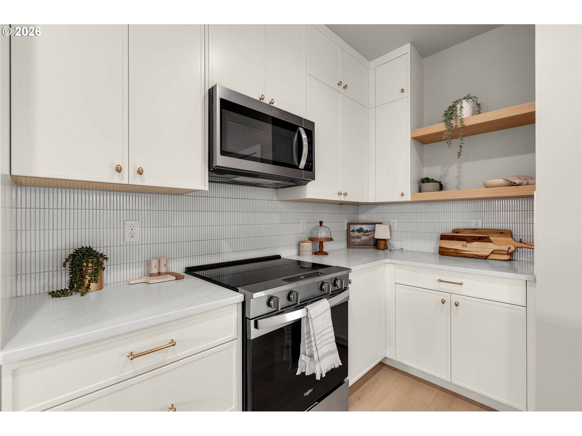Kitchen with white cabinets, brass hardware, vertical tile backsplash, and stainless-steel range.