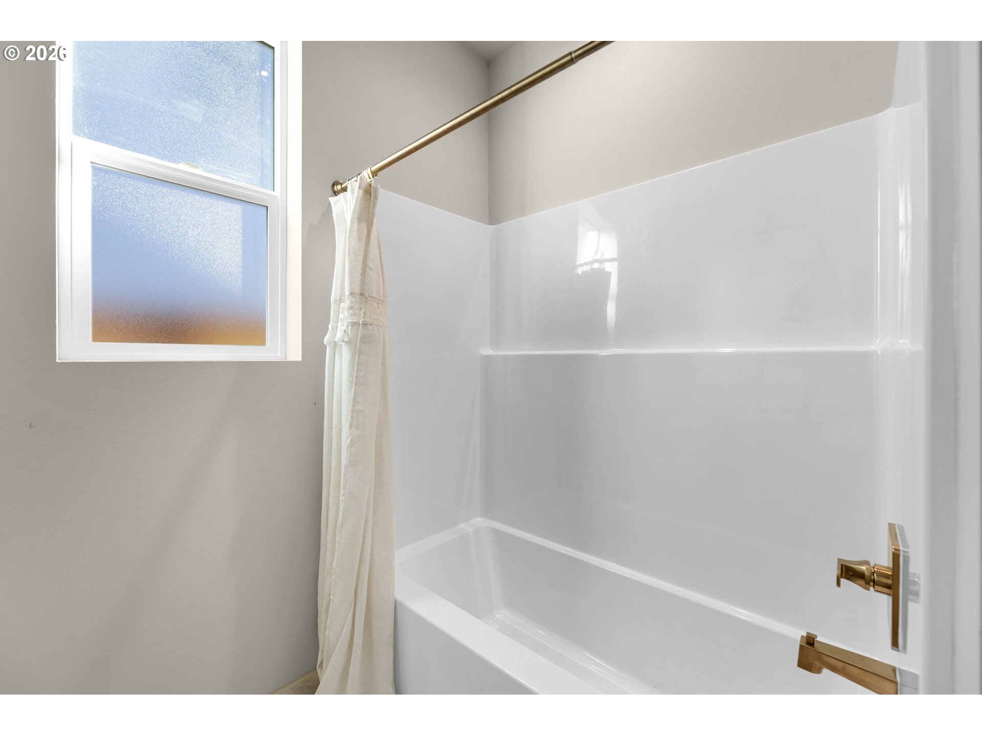 Bathroom with a white bathtub, brass fixtures, and a window beside the shower curtain.