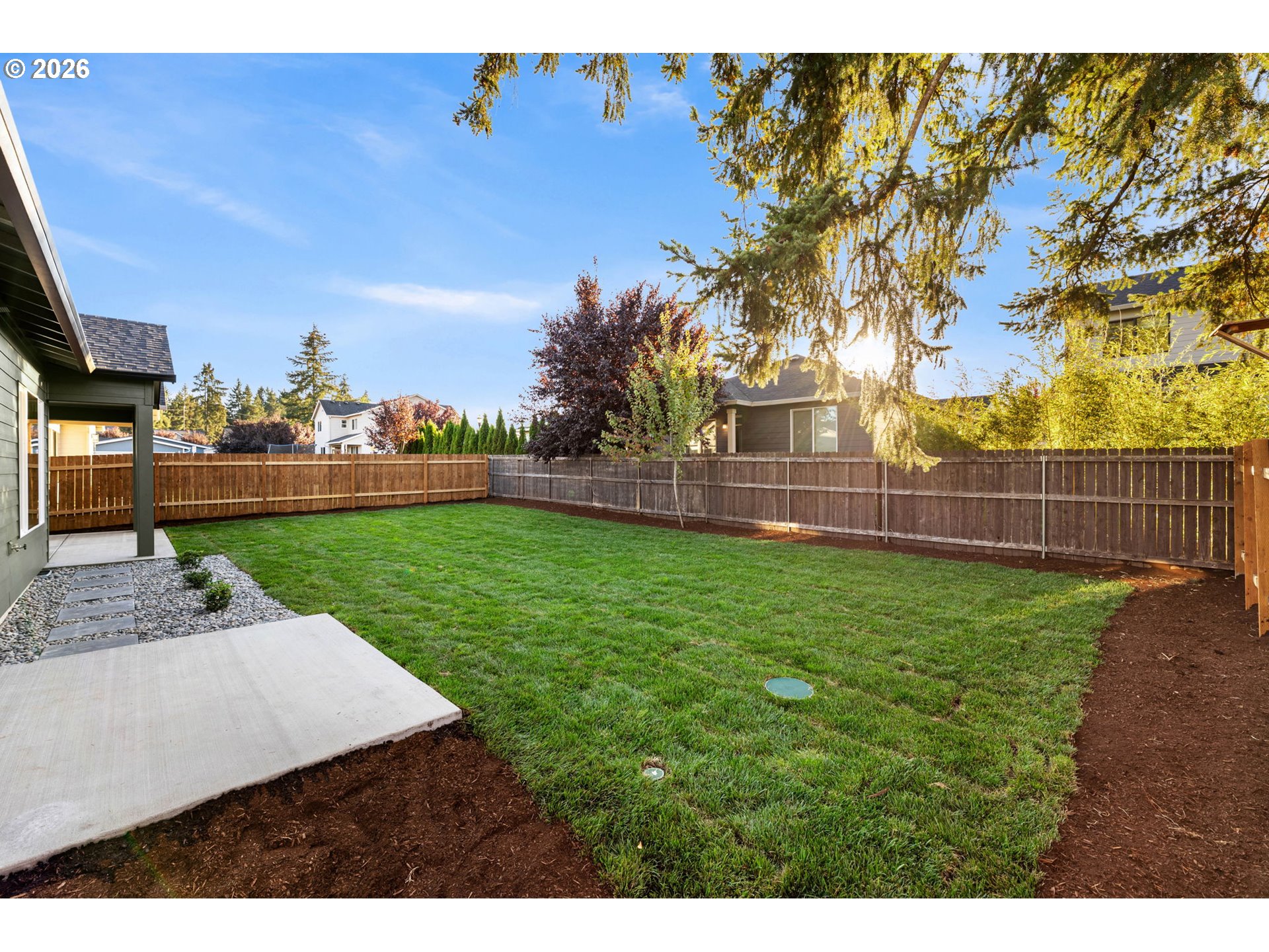 Fenced backyard with a broad green lawn, concrete patio, and mulched garden beds.