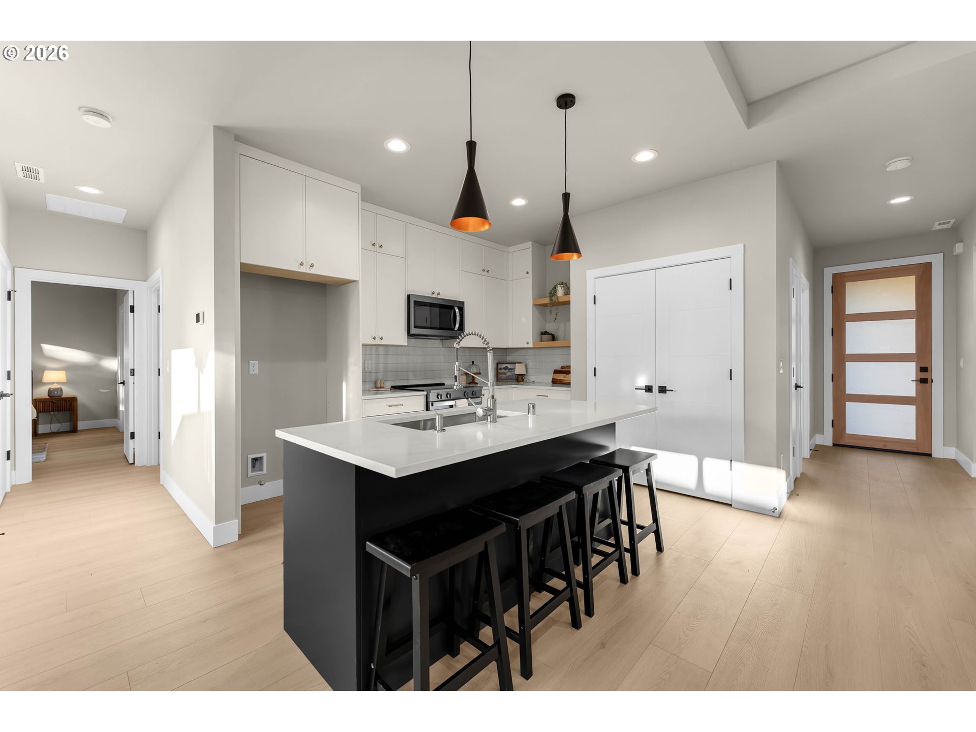 Modern kitchen with a large island, black bar stools, white cabinets, and light wood floors.