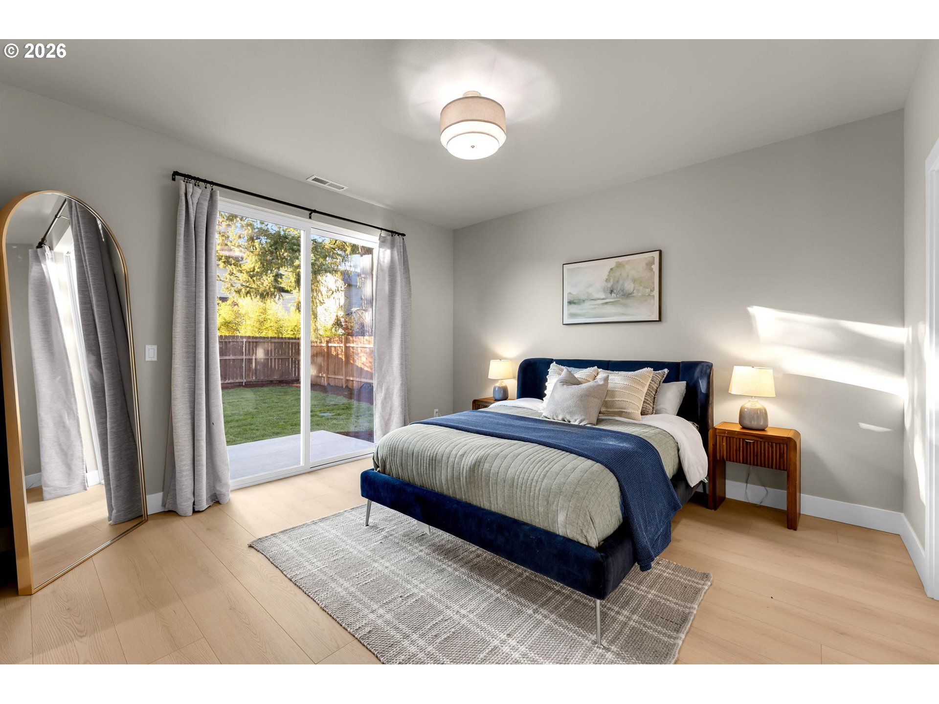 Staged bedroom with a navy bed beside sliding glass doors opening to a fenced backyard.