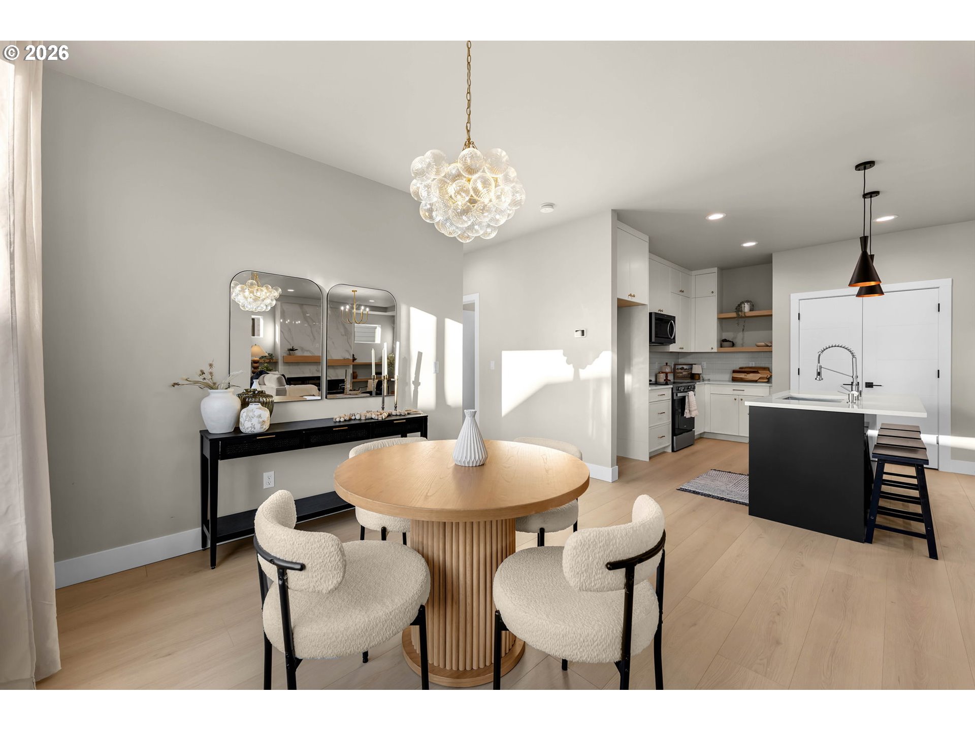 Dining area with a round wood table and upholstered chairs opening into a bright kitchen.