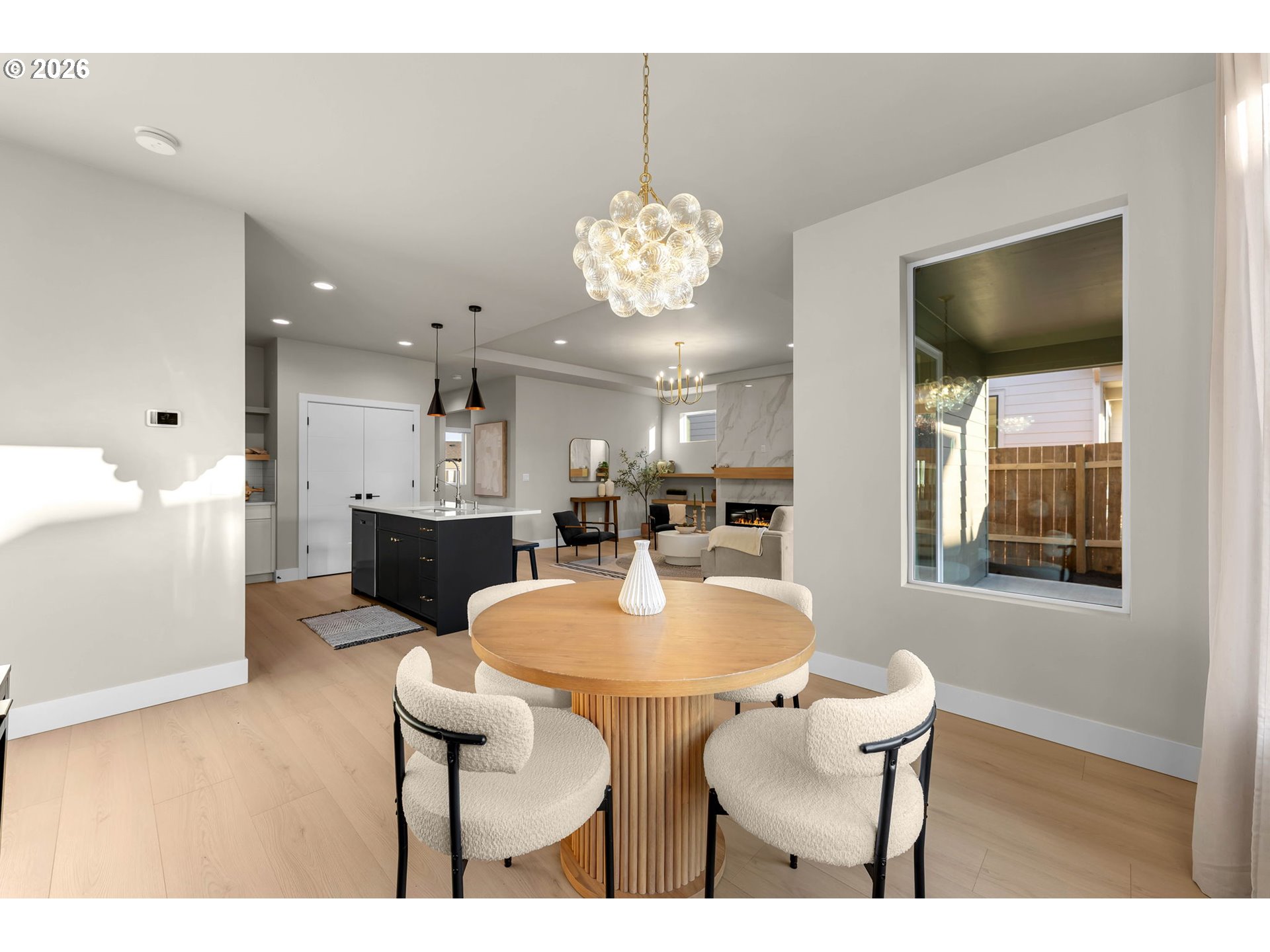 Open-plan dining area with a round wood table beneath a glass globe chandelier.