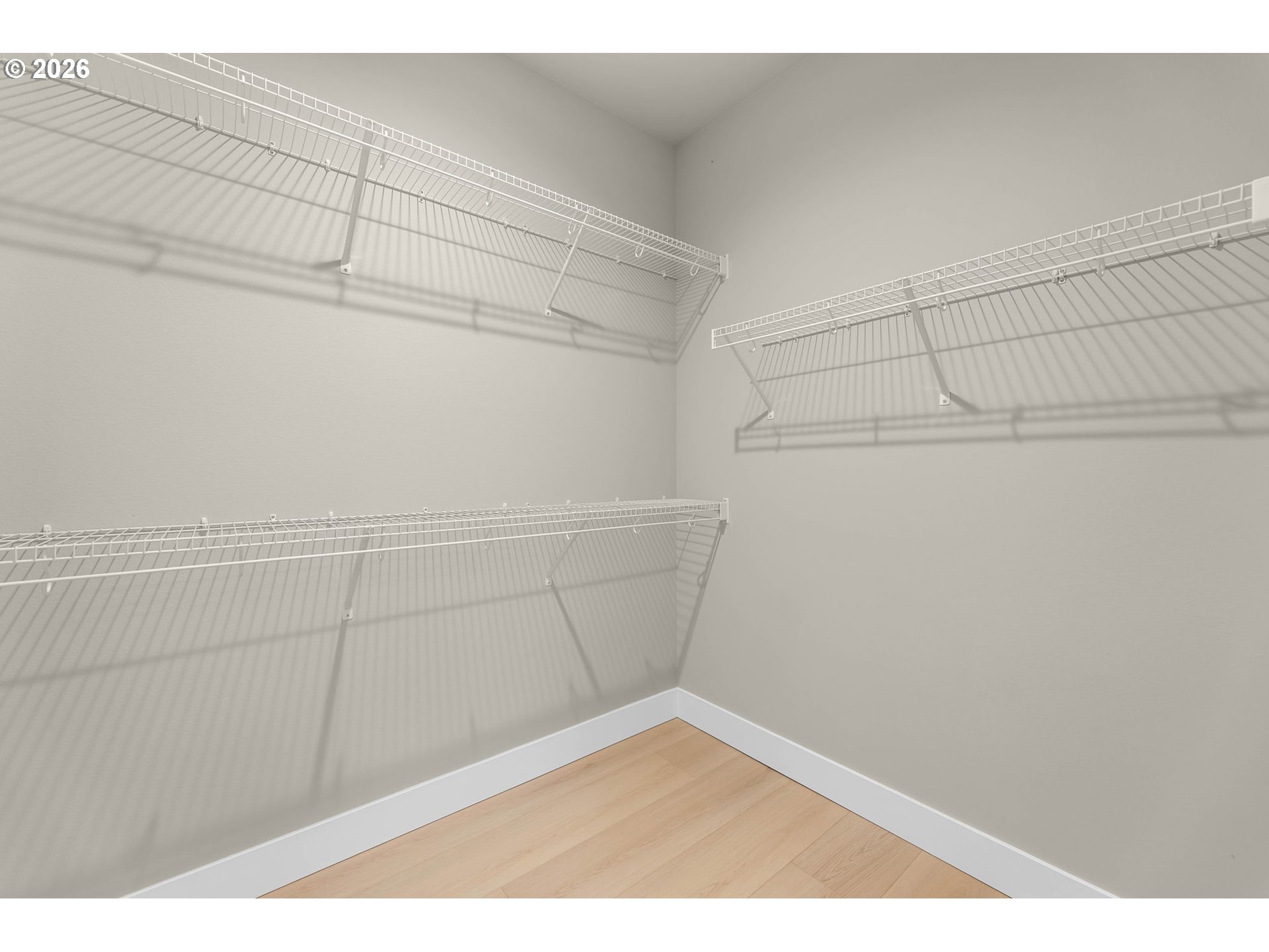 Empty walk-in closet with white wire shelving on three walls and light wood flooring.