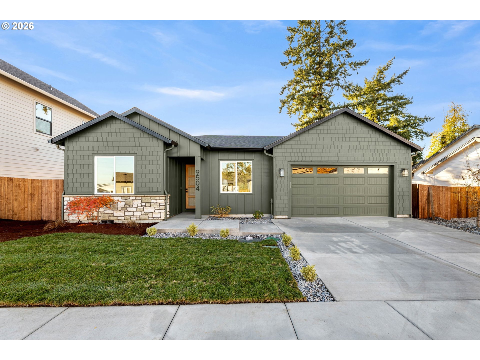 Gray-green single-story home with stone veneer, a two-car garage, and landscaped front lawn.